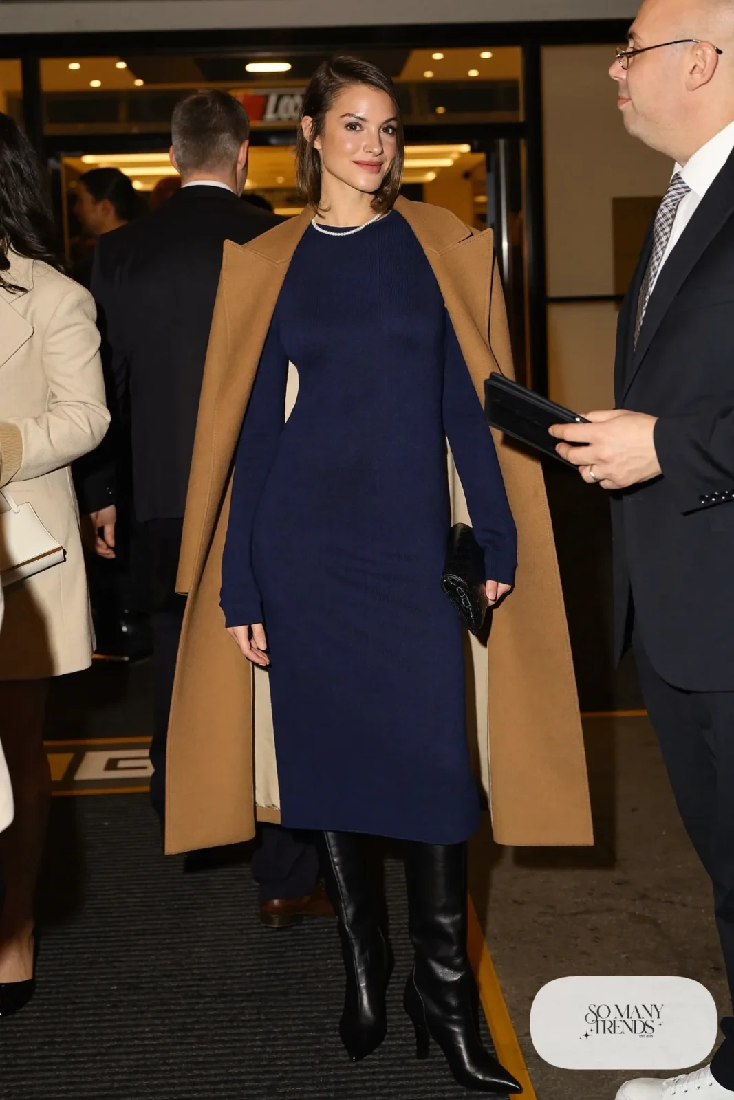 Woman in navy knit midi dress, camel wool cape, black tights and knee-high boots, hockey game outfit 27