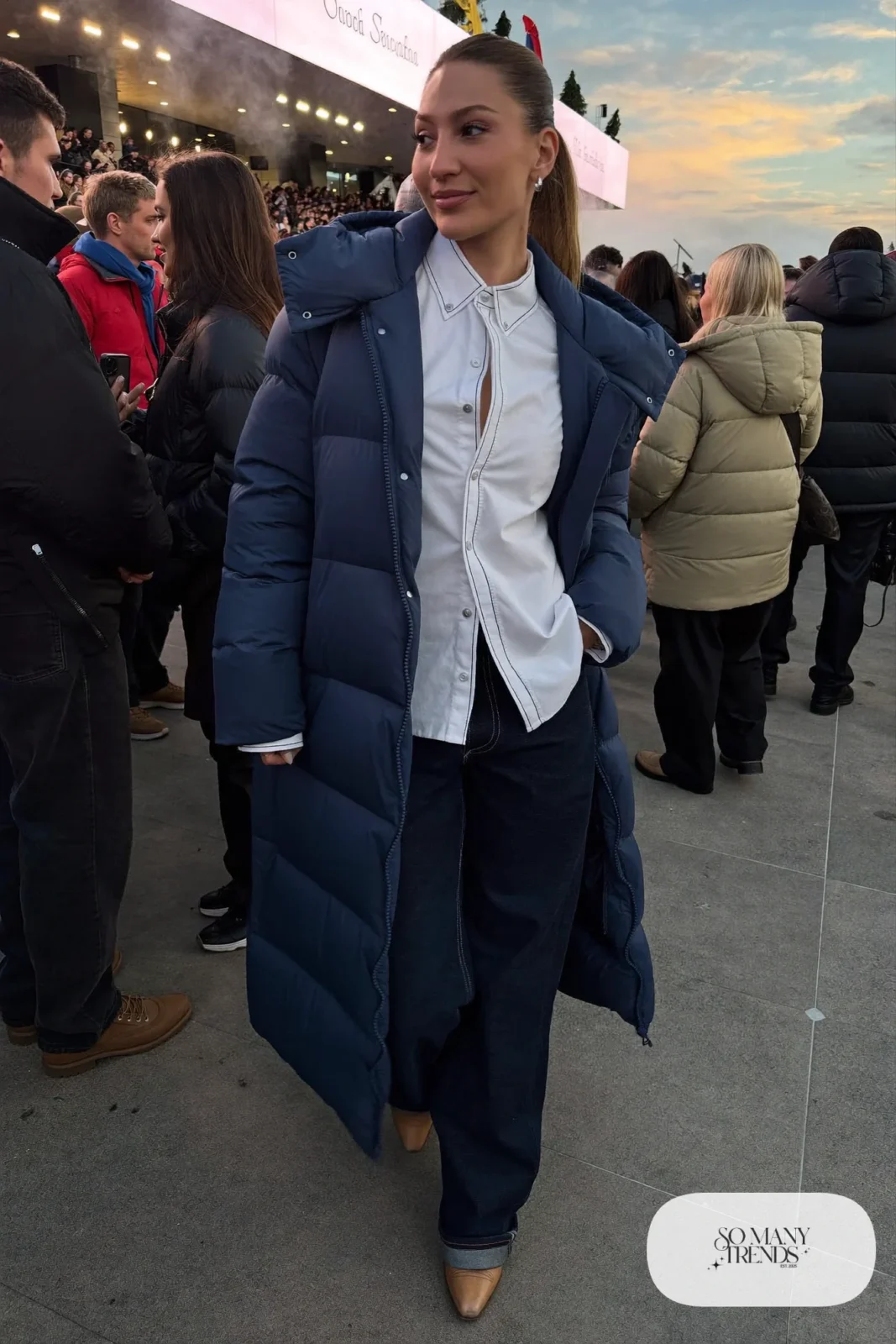 Woman in a navy long puffer coat, white western snap shirt, dark jeans and tan boots, concert outfit 5