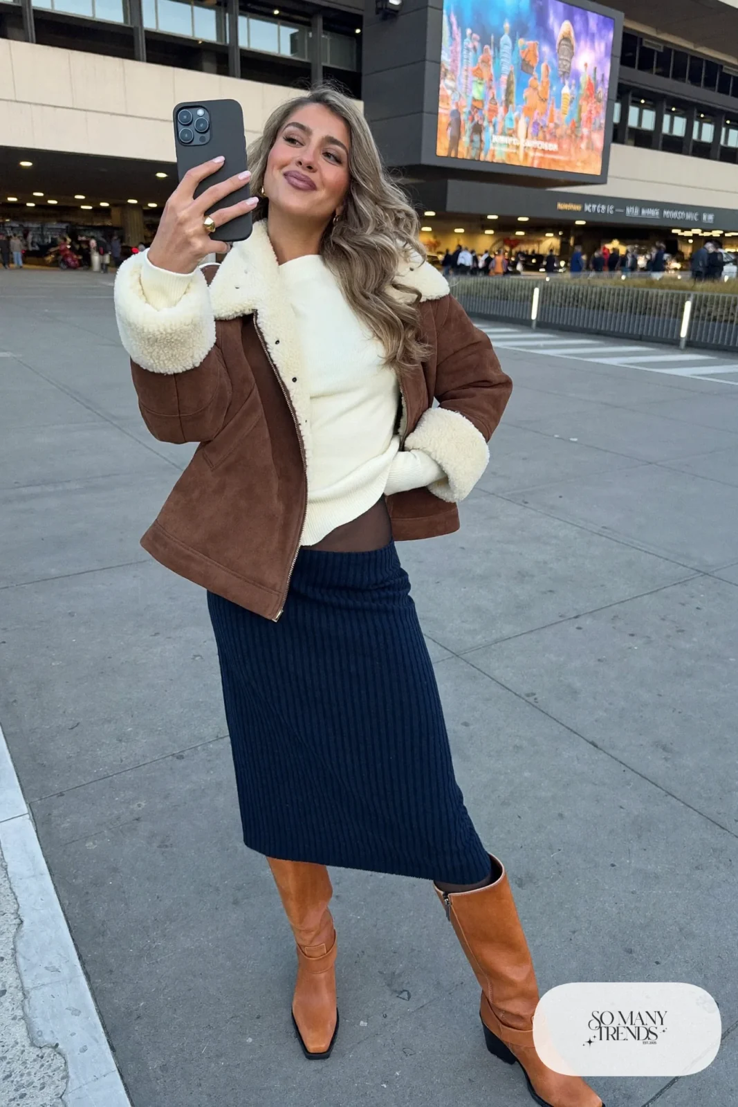 Woman in a navy knit midi skirt, cream sweater, cropped shearling jacket and tall cognac boots, concert outfit 7