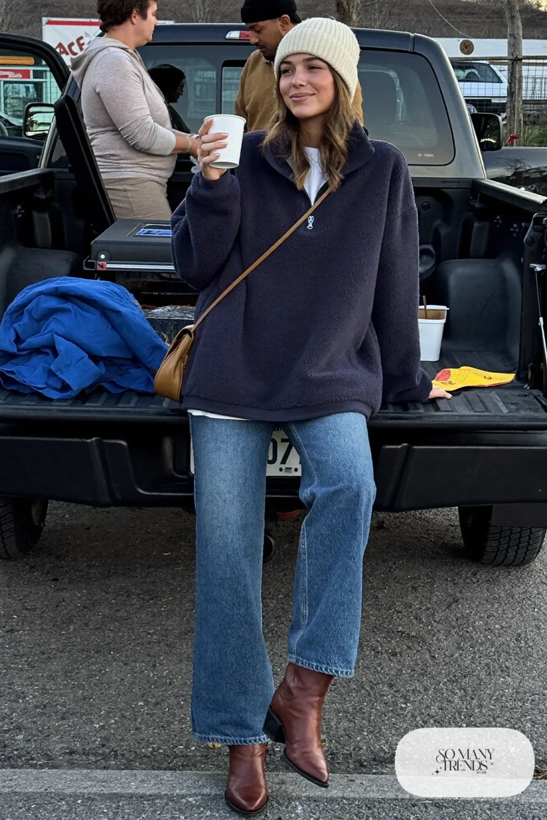Woman in a navy half-zip fleece pullover, barrel-leg jeans, brown boots and crossbody bag, concert outfit 15