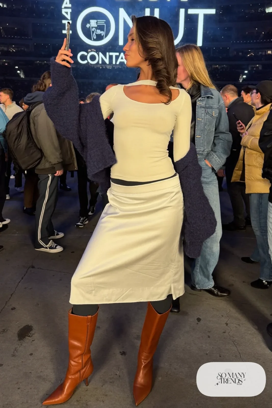 Woman in a white satin midi skirt, thermal top, chunky navy cardigan, tights and tall boots, concert outfit 18