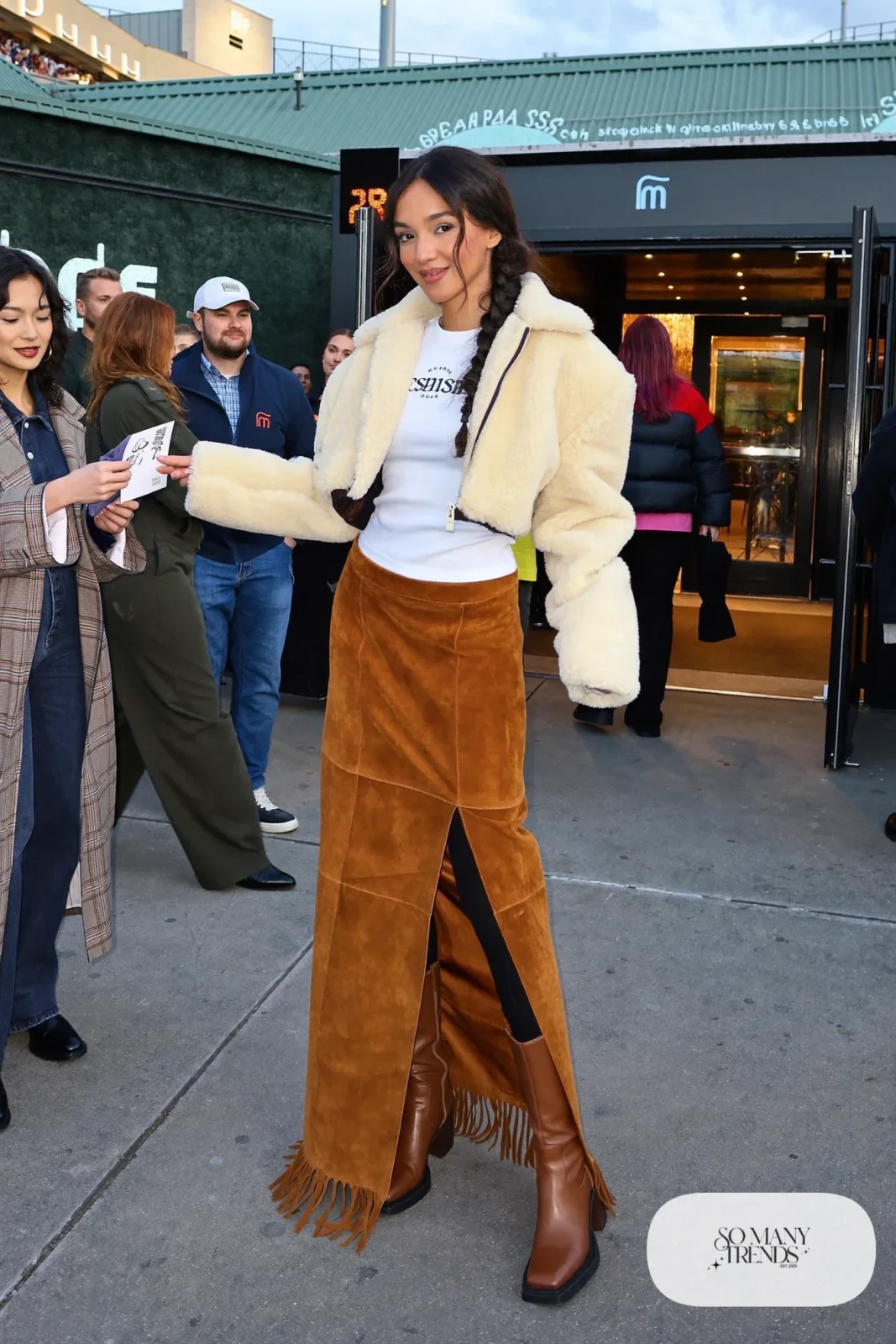 Woman in a cropped sherpa jacket, white thermal tee, cognac fringe maxi skirt and ankle boots, concert outfit 26