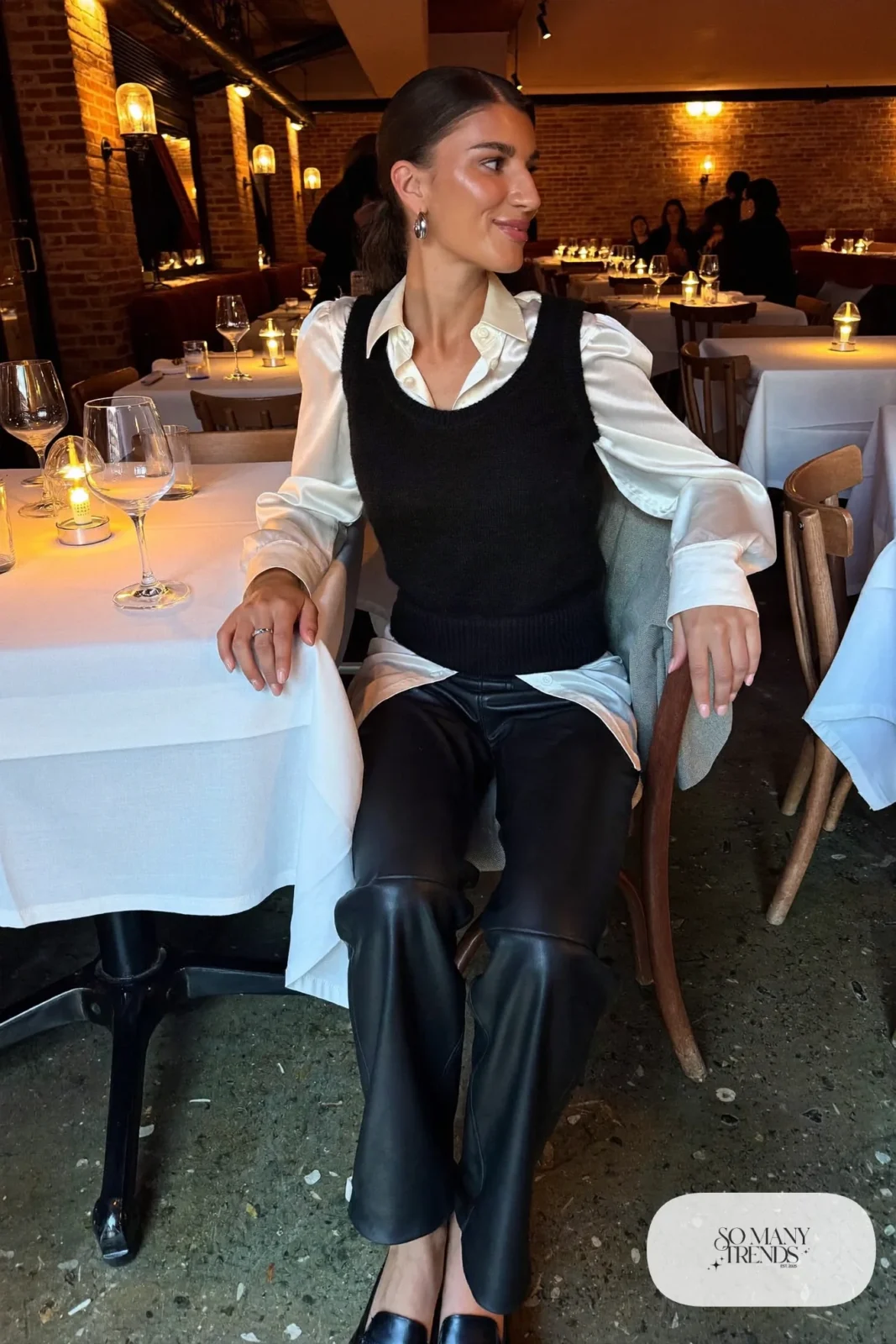 Woman in a black knit sweater vest over a pearl silk blouse with black faux leather pants and black loafers at a mountain town dinner, outfit 21
