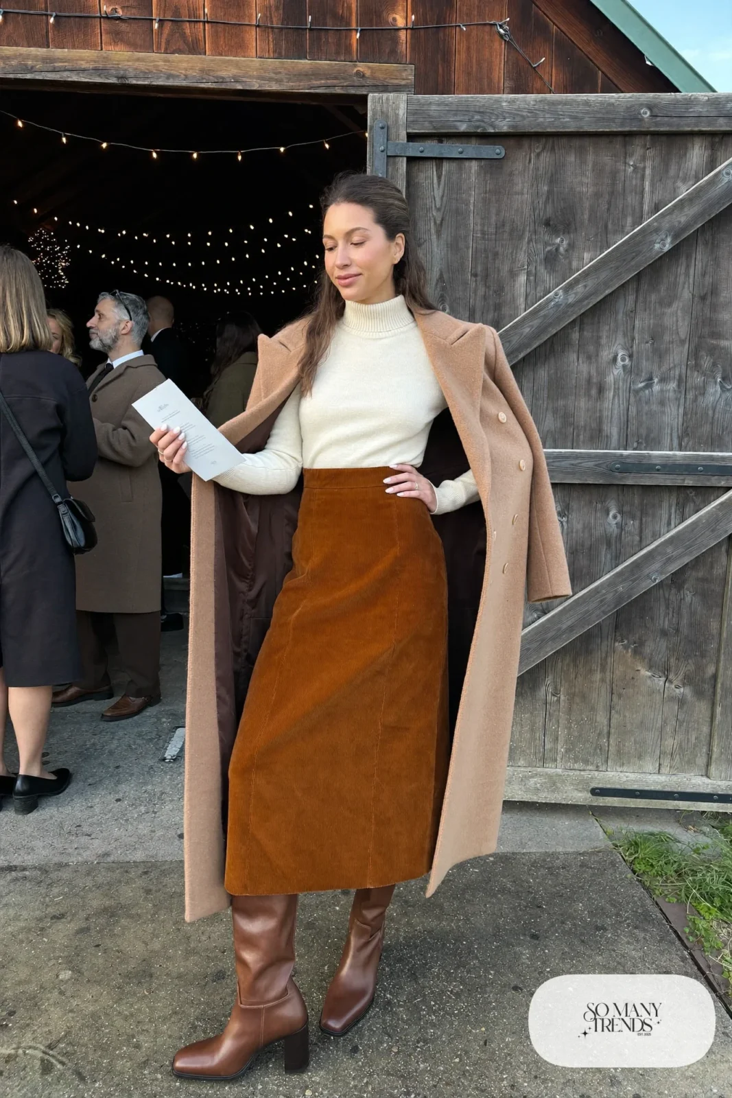 rust corduroy midi skirt, cream merino turtleneck, camel wool coat, brown tall block-heel boots, opaque tights, winter wedding guest outfit 1