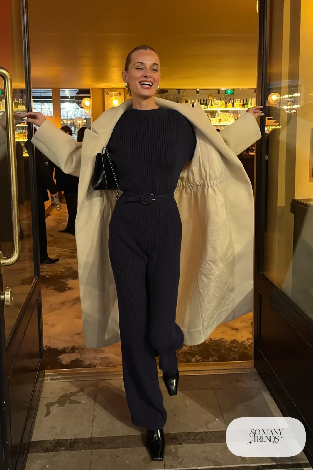 Look 18: navy knit wide-leg jumpsuit, long cream wool coat, black leather ankle boots and a small black bag