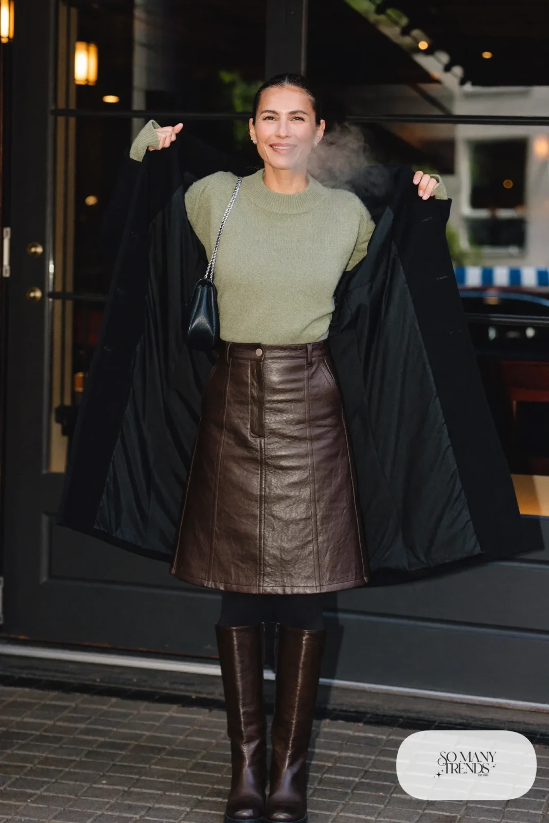 Look 31: chocolate brown leather midi skirt, sage green knit sweater, black tights, tall brown boots and a long black coat