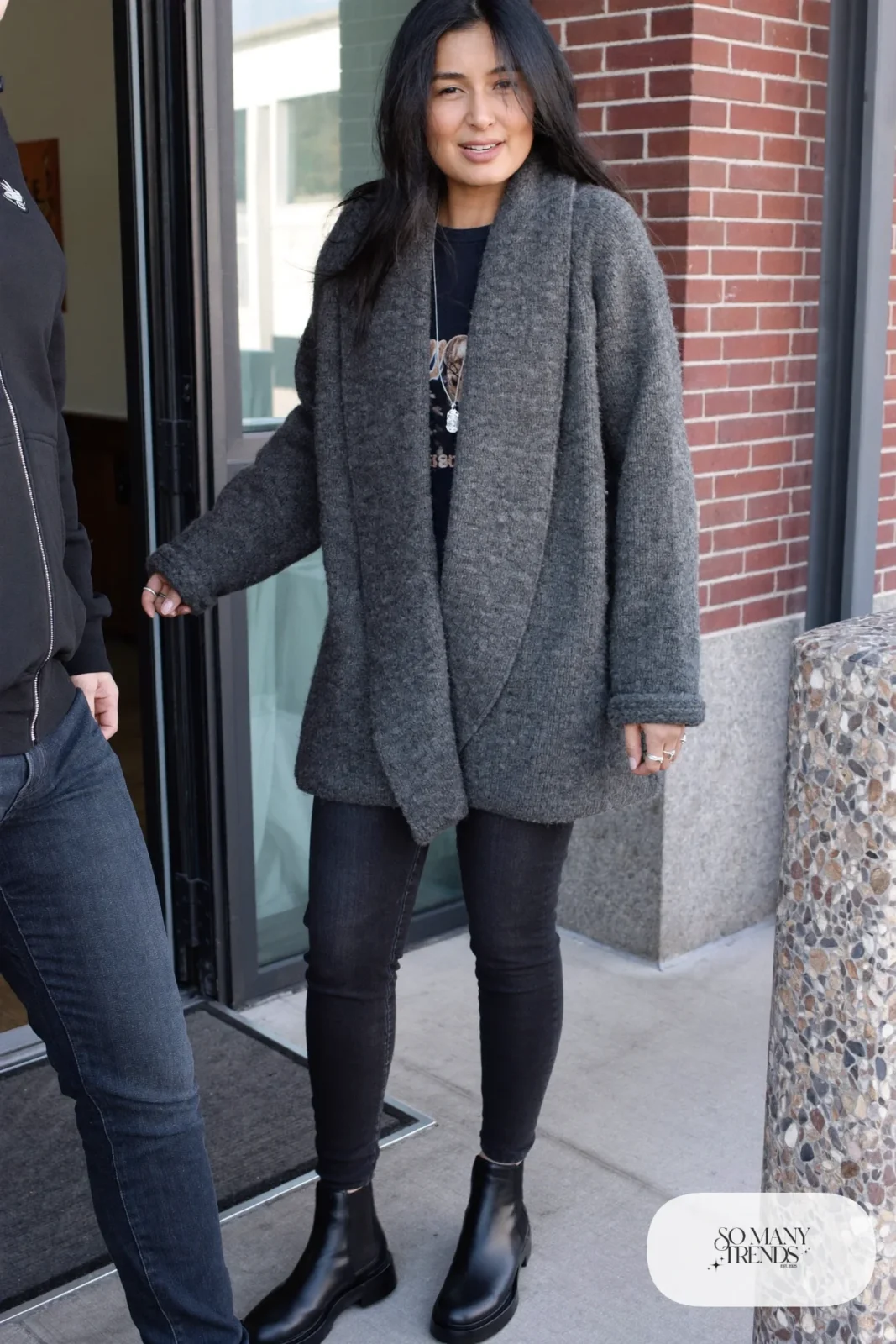 Woman in a charcoal chunky cardigan, black graphic tee, dark skinny jeans and black lug-sole Chelsea boots, outfit 5