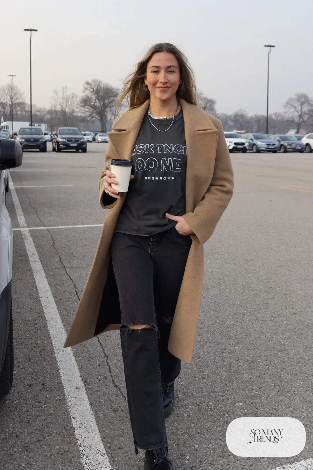 Woman in a camel wool coat over a band tee, ripped black jeans and black platform boots, outfit 6