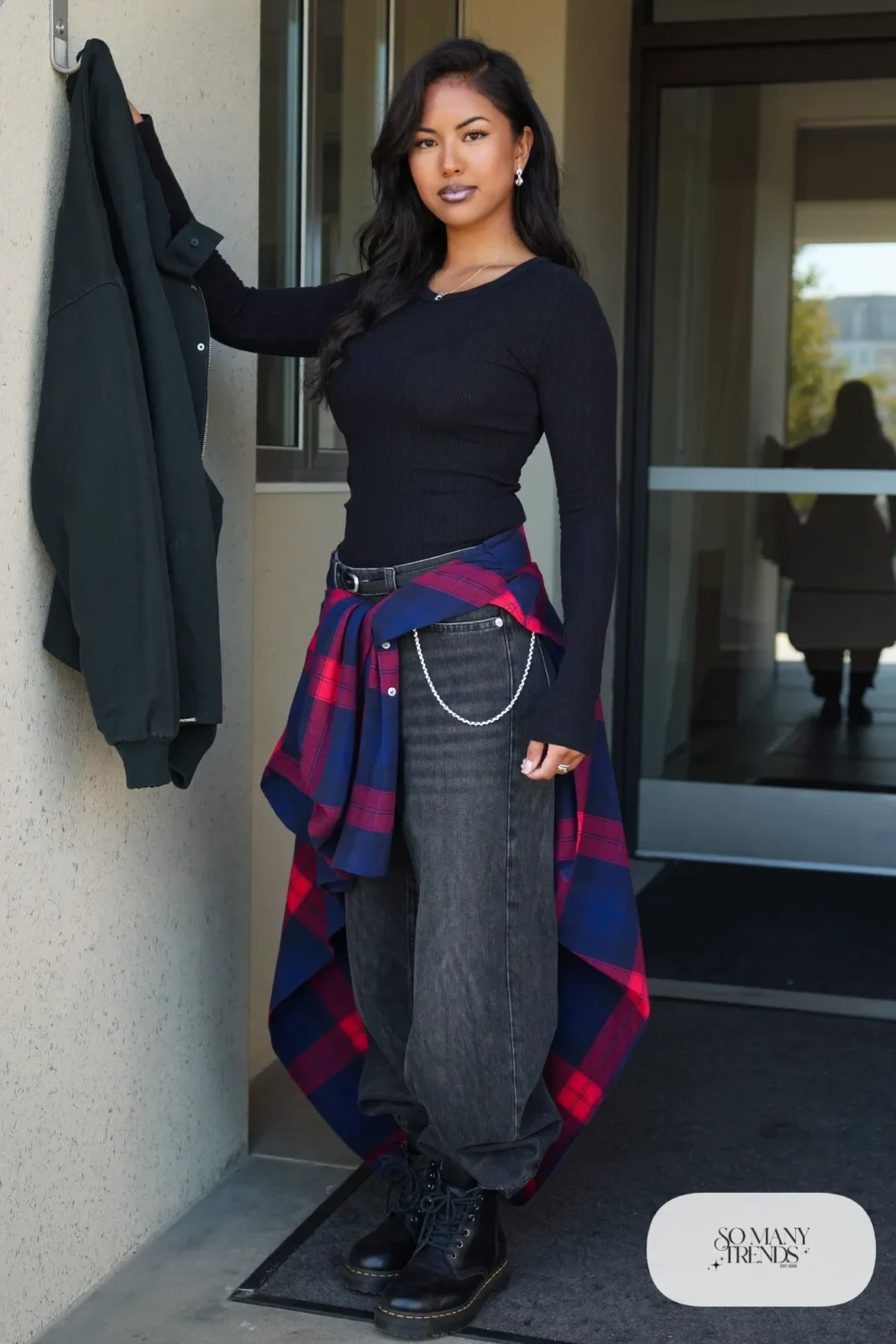 Woman in a long black thermal top, flannel tied at the waist, faded black bootcut jeans and combat boots, outfit 10