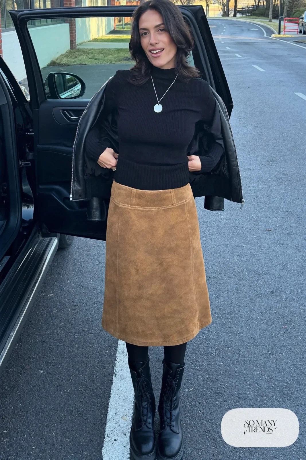Woman in a camel faux suede midi skirt, black sweater, leather jacket, thick tights and combat boots, outfit 16