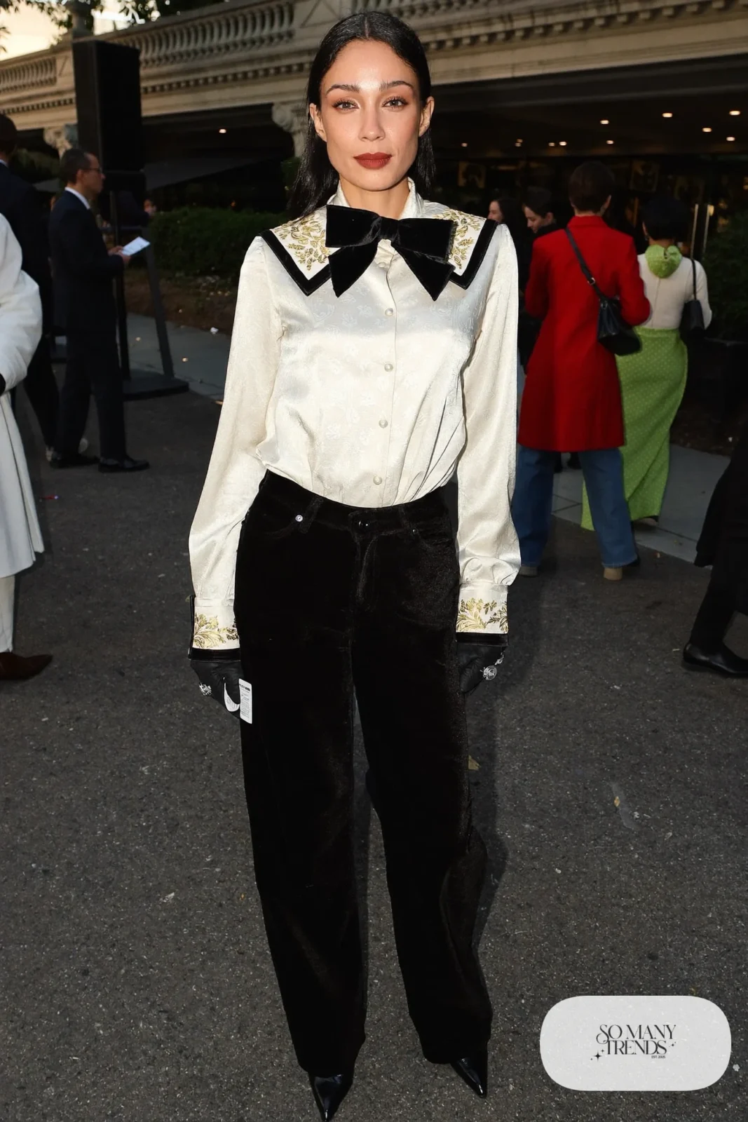 Woman in black velvet wide pants, cream bow blouse, black gloves and pointed black boots, outfit 20