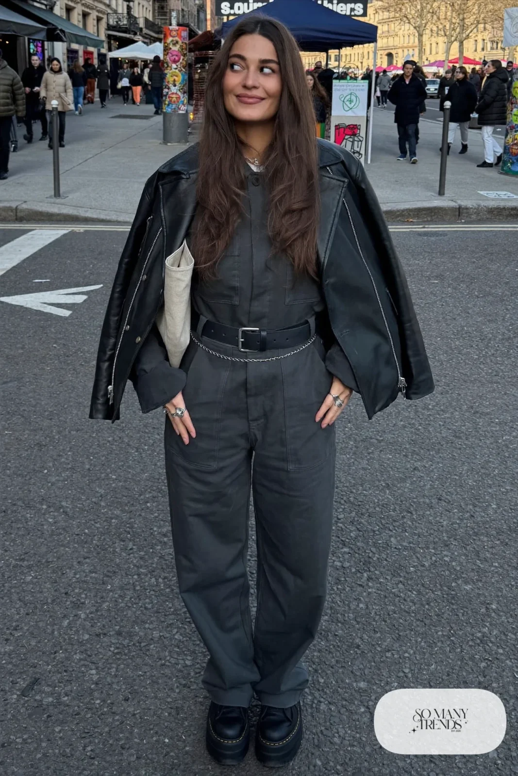 Woman in a charcoal utility jumpsuit, black leather jacket, silver chain belt and black platform sneakers, outfit 30