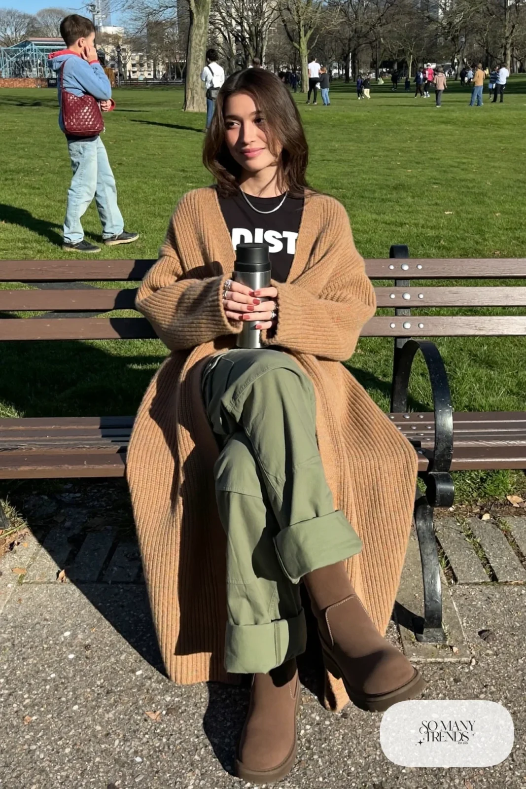 Woman in a long camel cardigan, black graphic tee, olive cargo pants and brown lug-sole boots, outfit 31