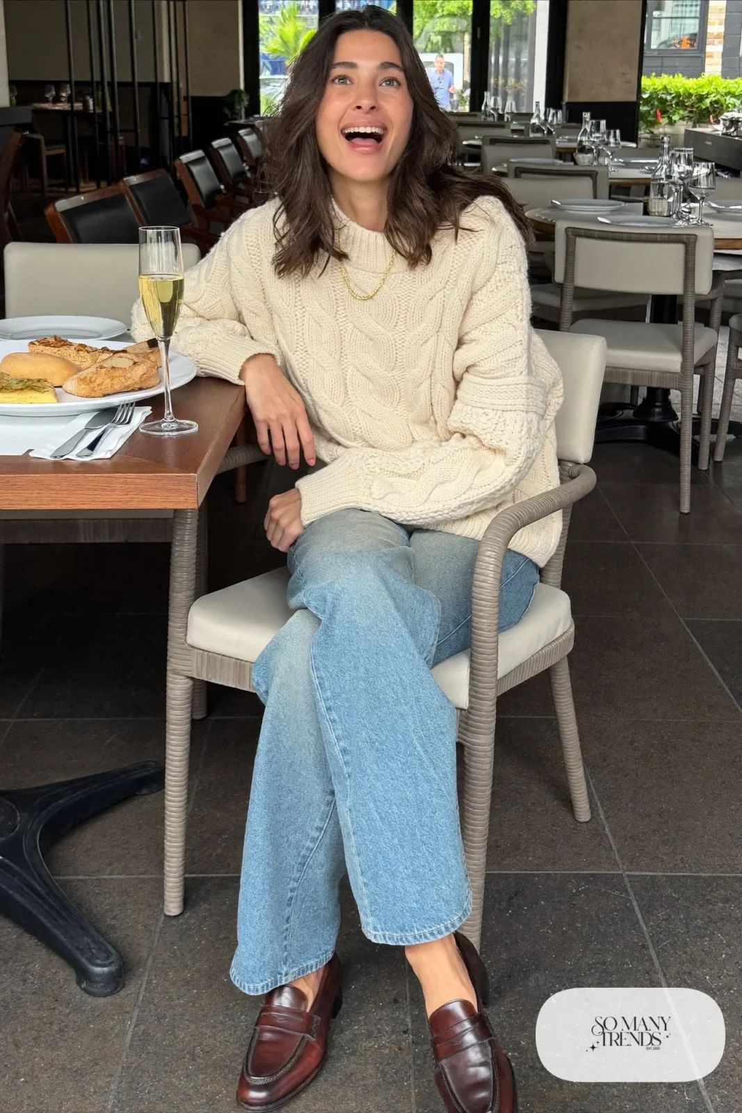 Woman in a cream cable-knit sweater, light baby blue straight jeans and brown loafers at a brunch table, outfit 4