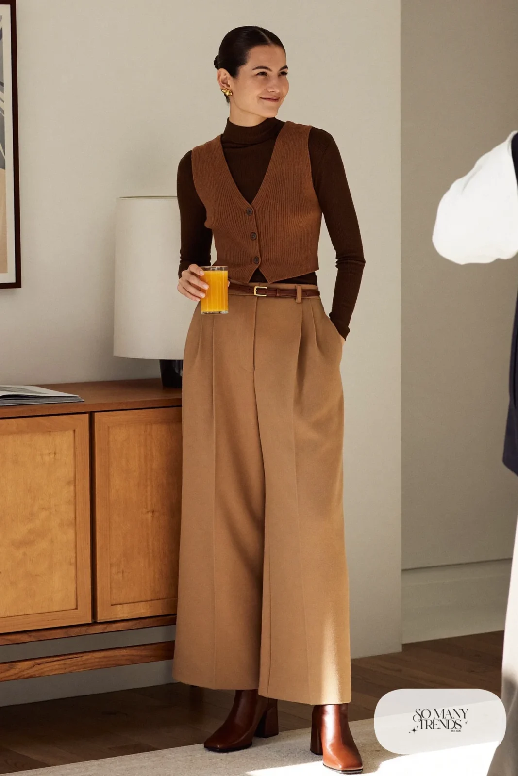 Woman in a brown fine-knit turtleneck with a camel knit vest, sand wide-leg pants and brown boots at a holiday table, outfit 5