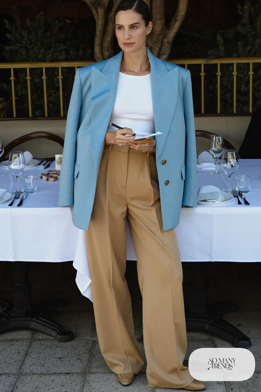 Woman in an oversized baby blue blazer, white tee, sand wide-leg pants and tan loafers in a restaurant, outfit 13