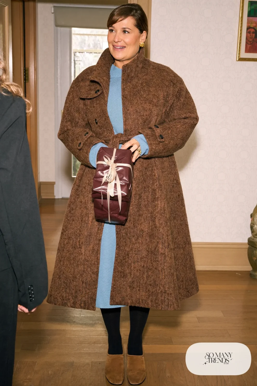 Woman in a long brown cardigan coat over a baby blue knit dress with tan suede boots at a front door, outfit 26