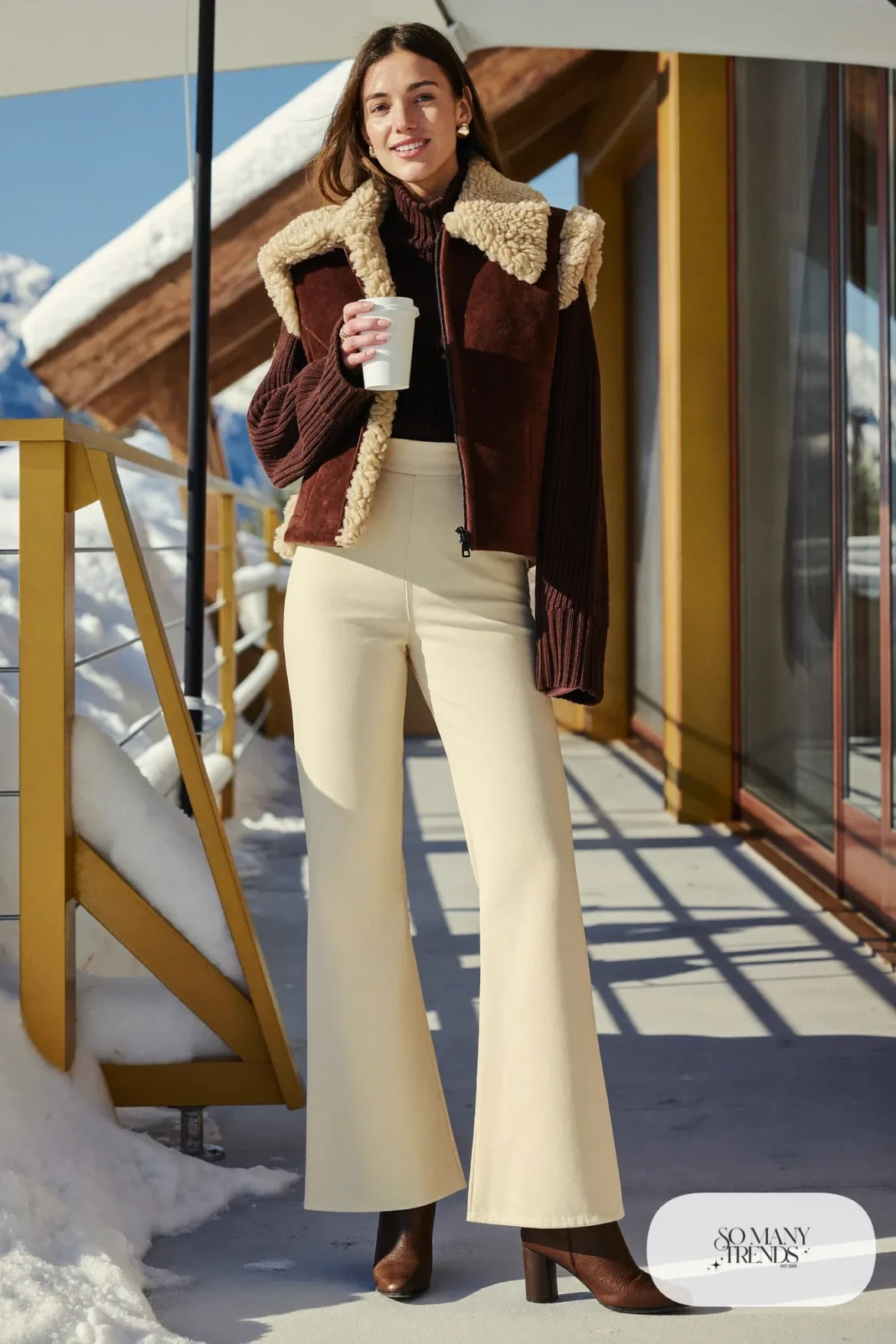 Woman in a cognac suede shearling vest, chocolate chunky turtleneck, cream flared pants and brown leather boots, outfit 16