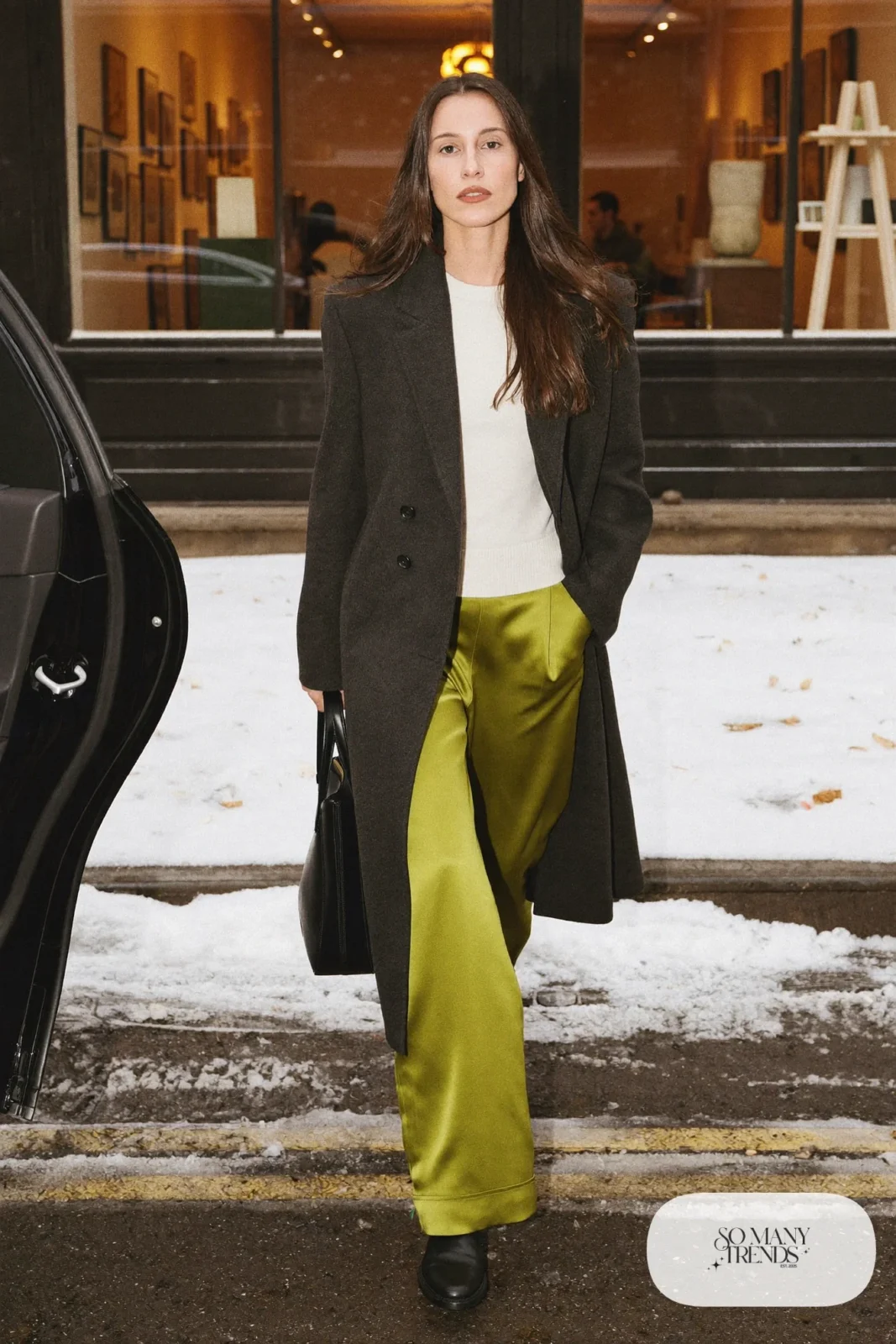 Woman in a charcoal tailored wool coat, cream knit top, moss green satin pants and black leather boots, outfit 17