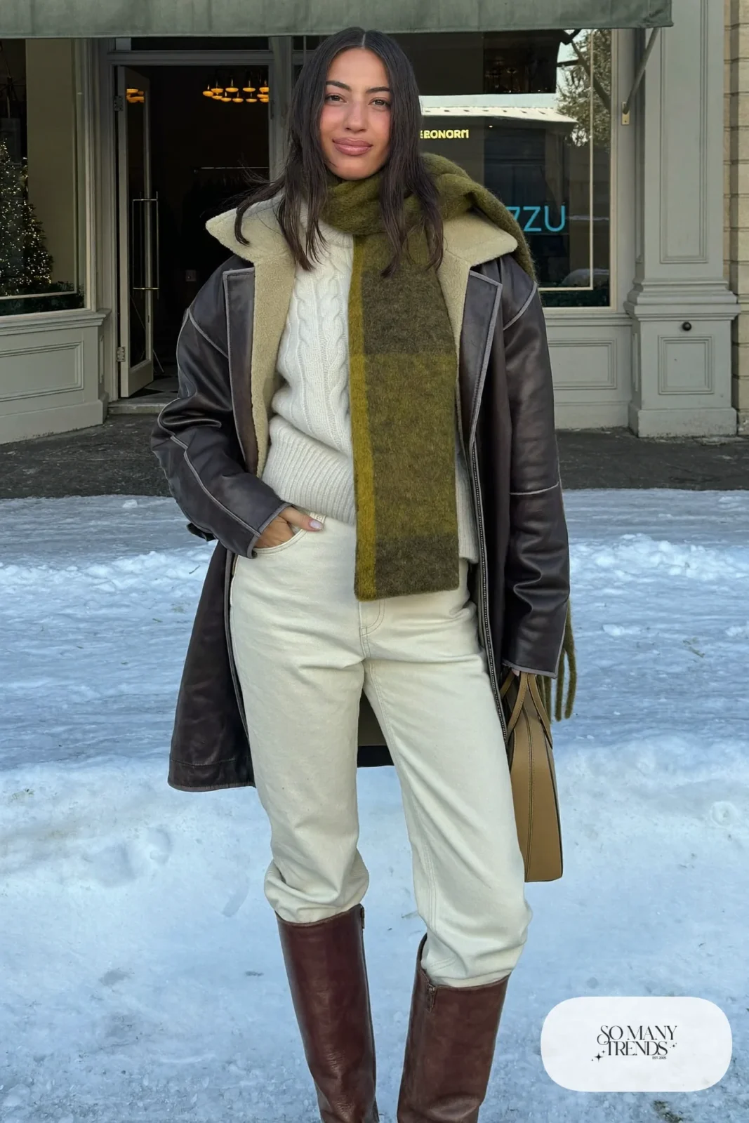 Woman in a chocolate leather jacket, cream straight jeans, moss green scarf and tall brown boots, outfit 24
