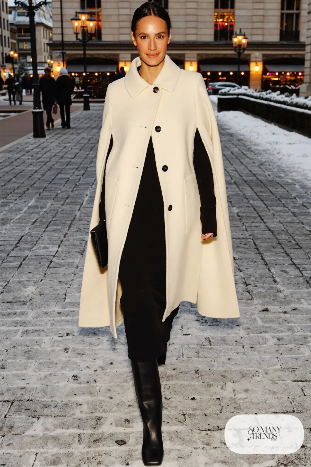 Woman in an ivory wool cape, black knit midi dress, black opaque tights and tall black boots, outfit 25
