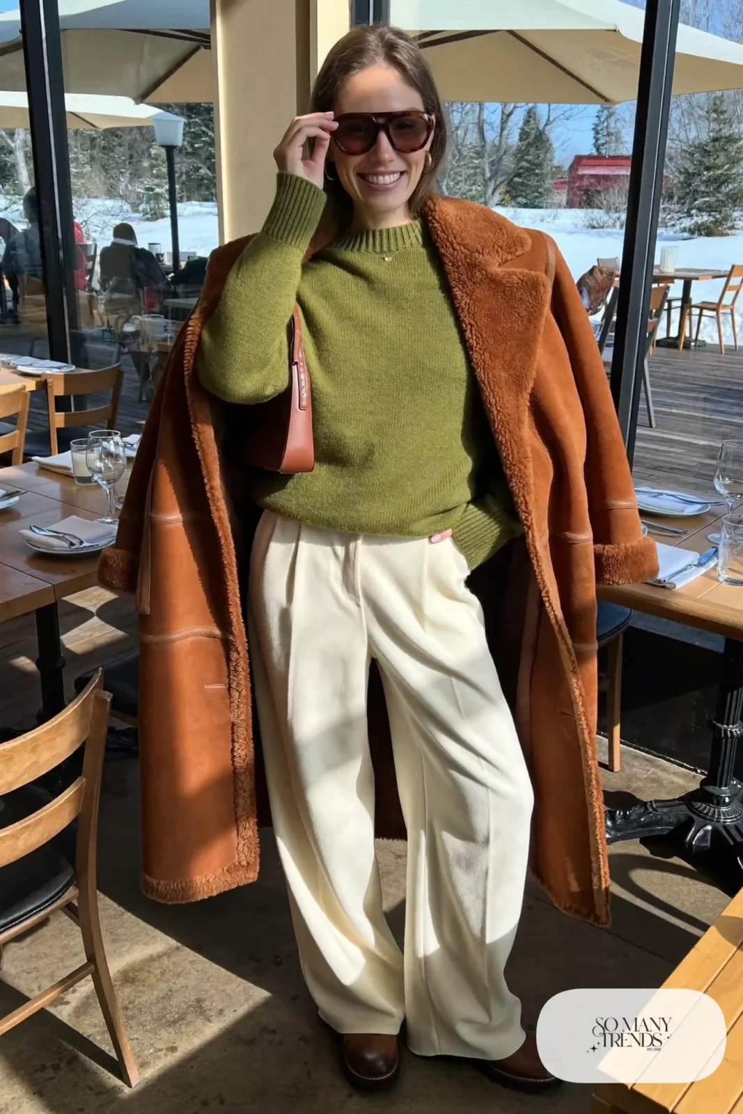 Woman in a cognac shearling coat, moss green knit sweater, cream wool wide-leg pants and brown leather boots, outfit 28