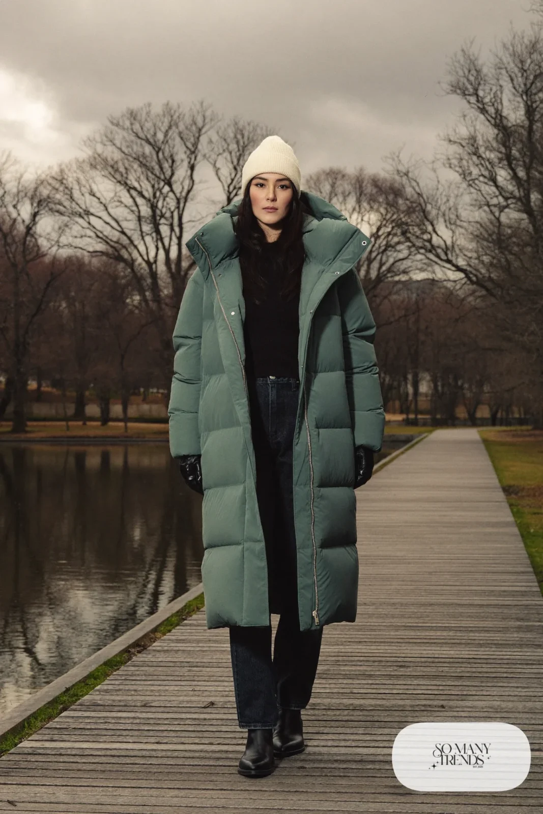 Woman in a long matte teal puffer coat, black jeans, black boots and a beige knit beanie, outfit 9