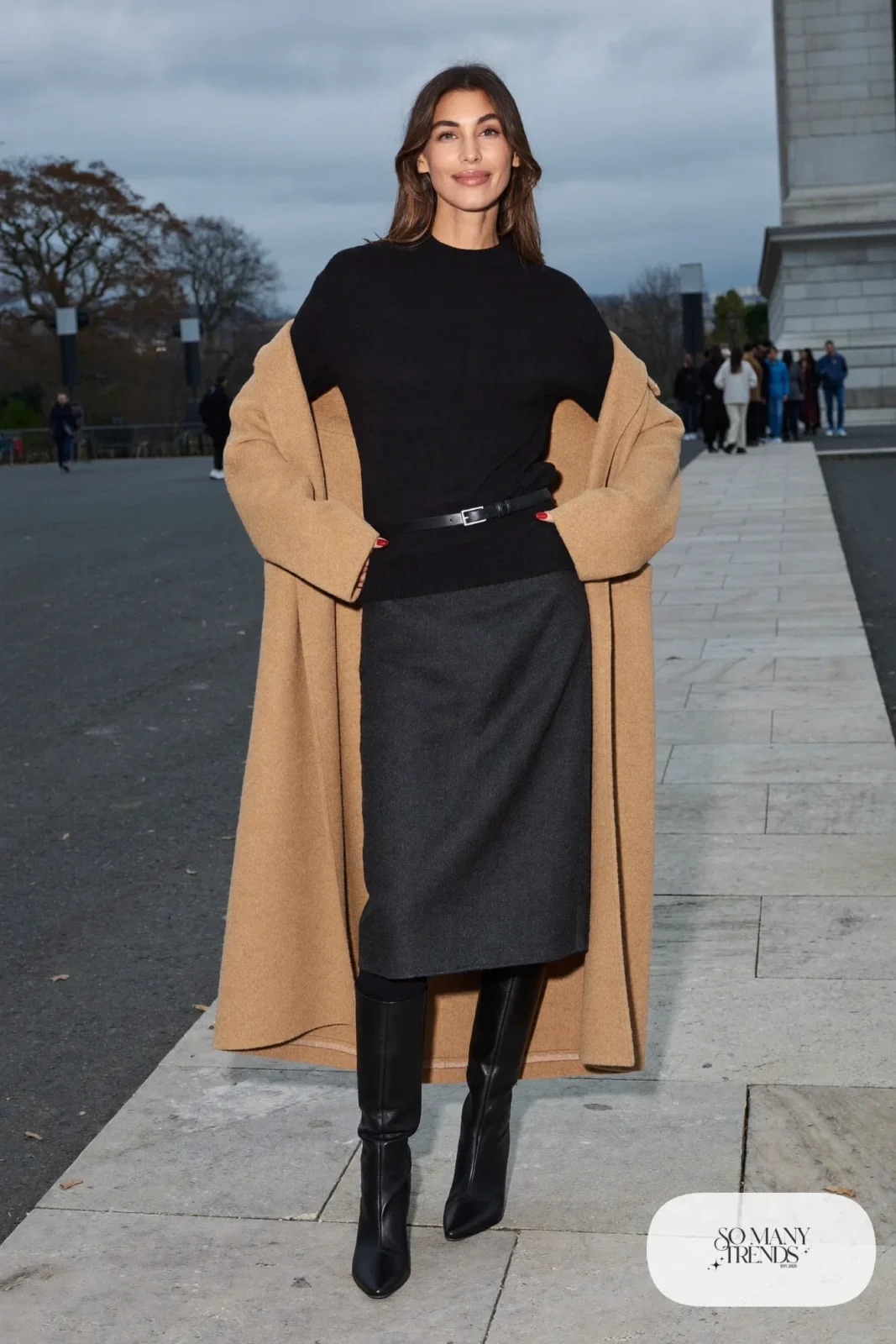 Woman in a charcoal midi wool skirt, black fitted sweater, black tights, tall black boots and a camel coat, outfit 10