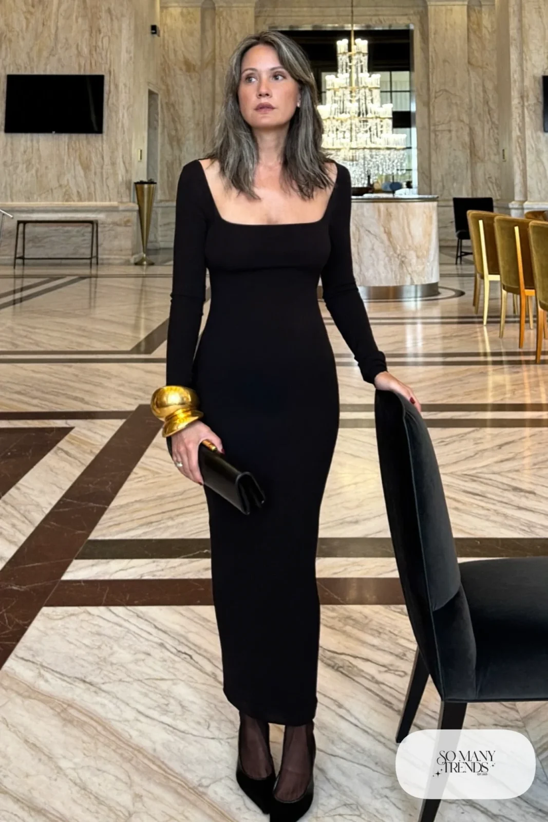 Woman in a black crepe long-sleeve column maxi dress with an oversized gold cuff bracelet and black pointed slingbacks, outfit 3