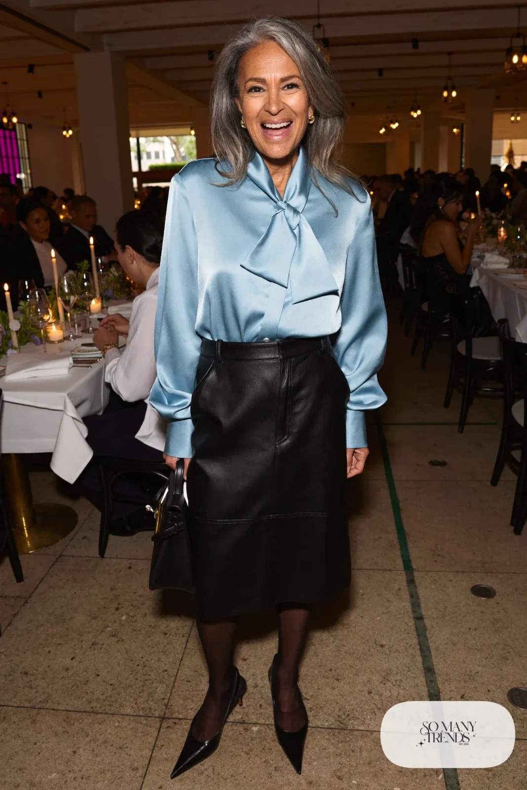 Woman in a powder blue satin bow blouse, black faux leather midi skirt, sheer black tights and black pumps, outfit 9
