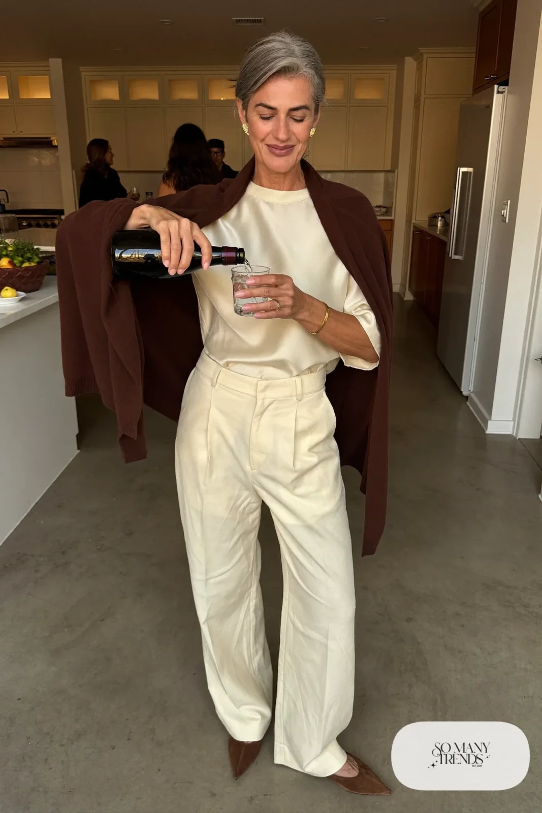 Woman in a chocolate brown cashmere wrap cardigan, cream silk top, cream wide-leg pants and brown suede flats, outfit 25