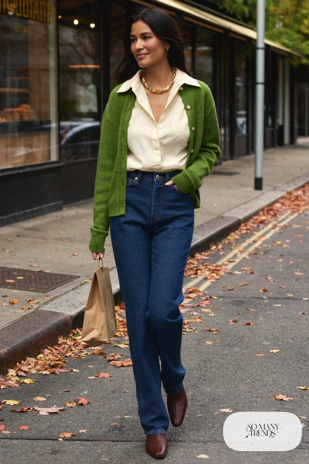 Woman in dark indigo straight-leg jeans, cream silk-look blouse, pine green cardigan and brown leather ankle boots, outfit 1