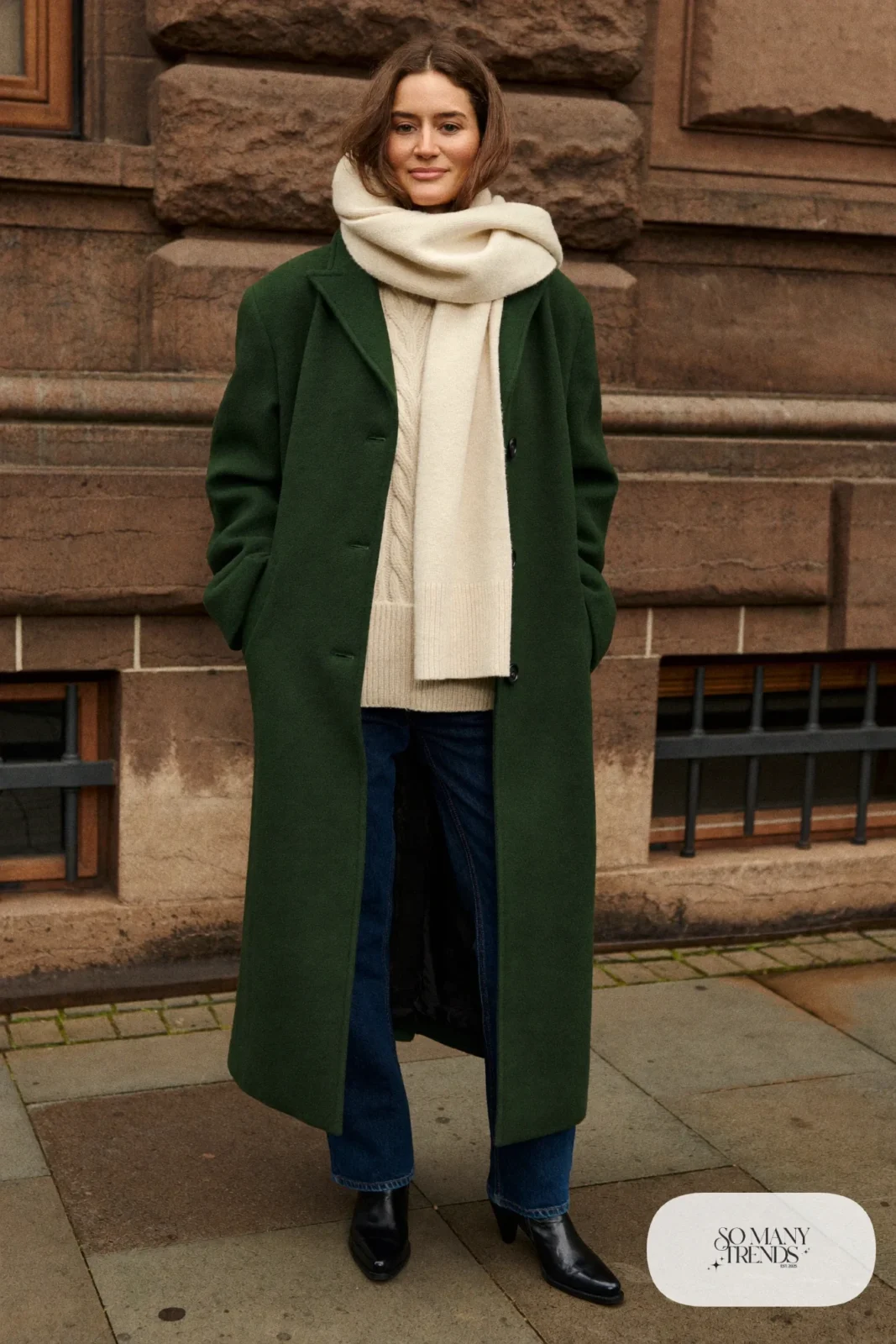 Woman in long pine green wool coat, oatmeal knit, straight jeans and black boots, outfit 6