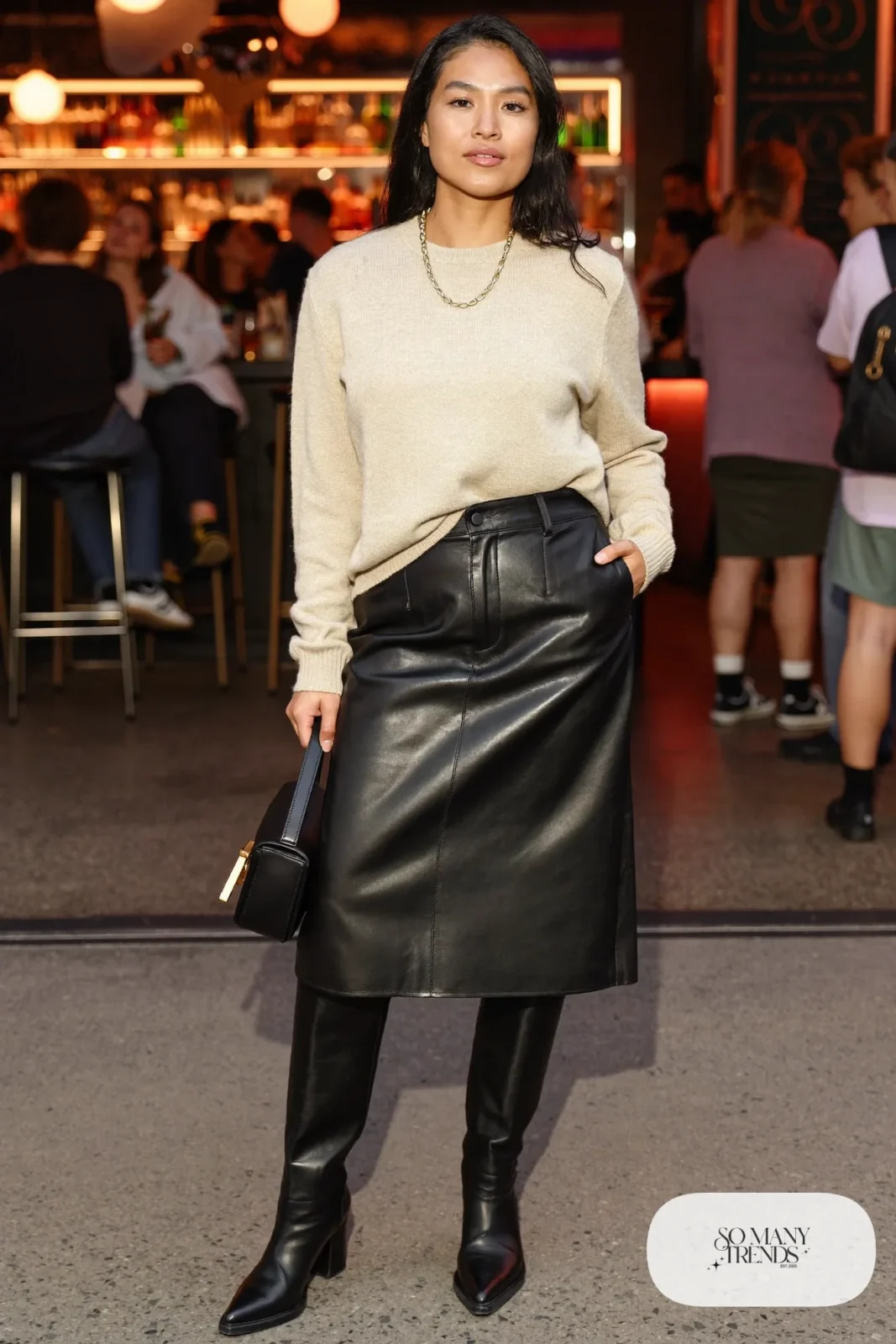 Woman in a black faux leather midi skirt with an oatmeal fine knit sweater and pointed black boots, photo 26