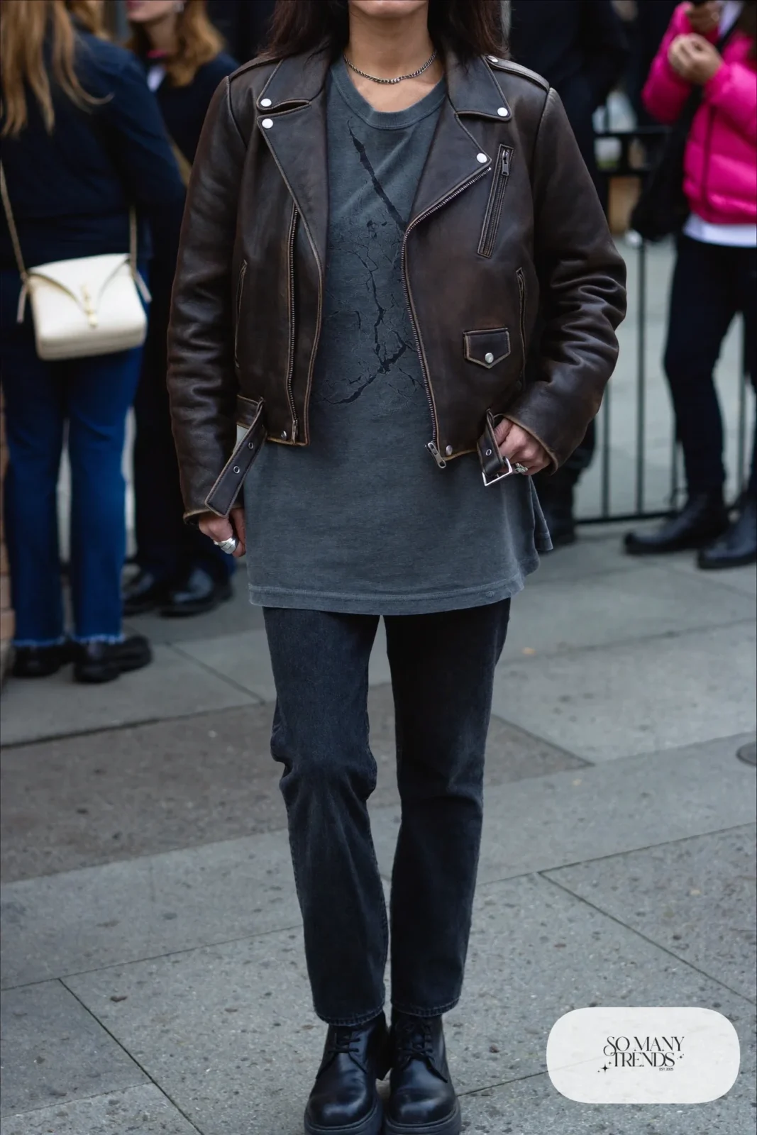 Woman in a black leather moto jacket, faded band tee, dark straight jeans and black combat boots, outfit 1