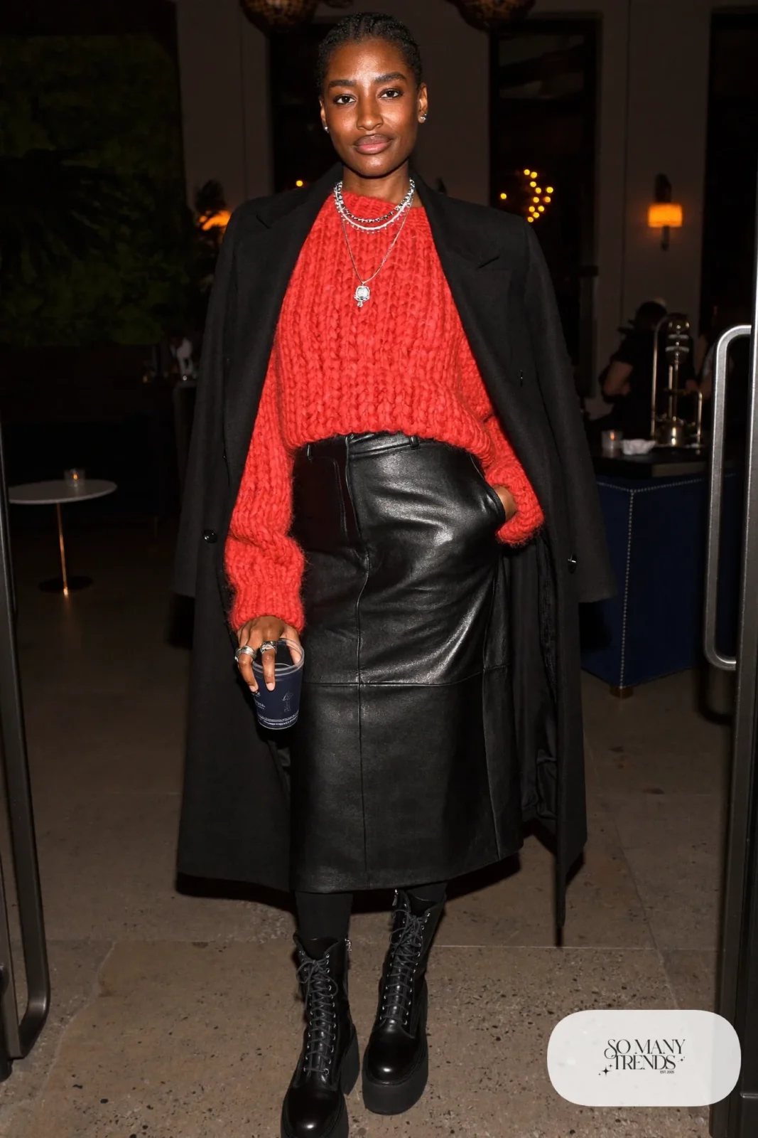 Woman in a tomato red chunky knit, black faux leather midi skirt, thick tights and black platform boots, outfit 25