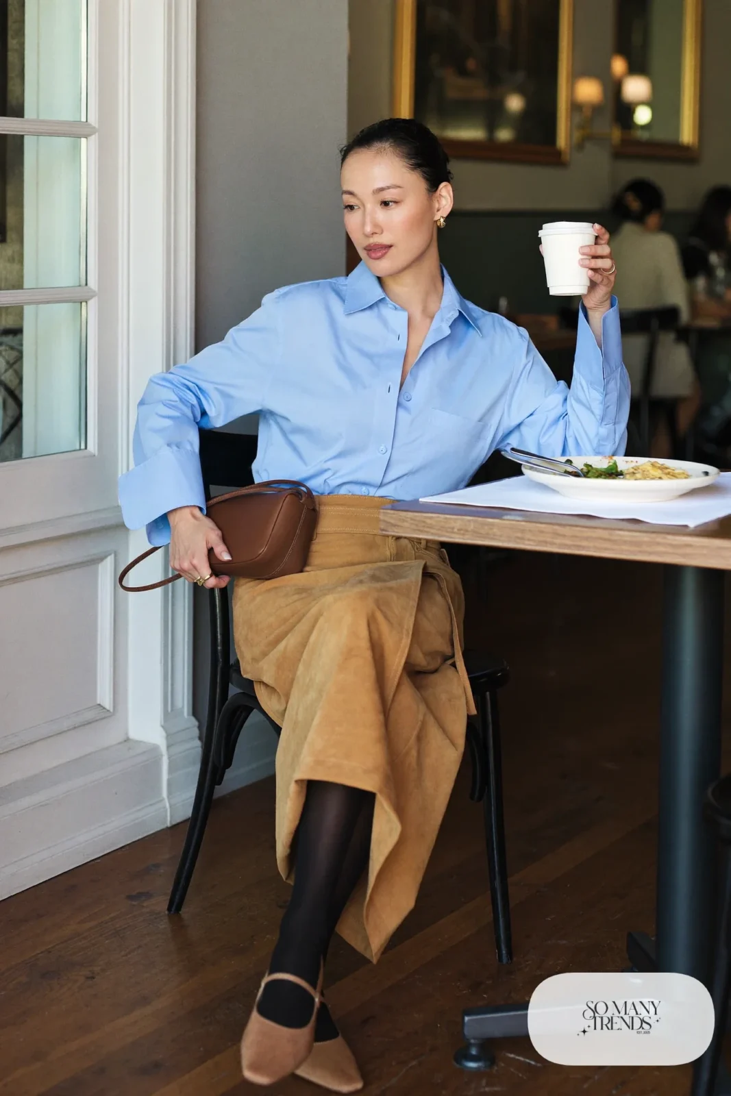 Woman in a baby blue button-down shirt, camel wrap midi skirt, slingback flats and a brown bag at a restaurant, outfit 10