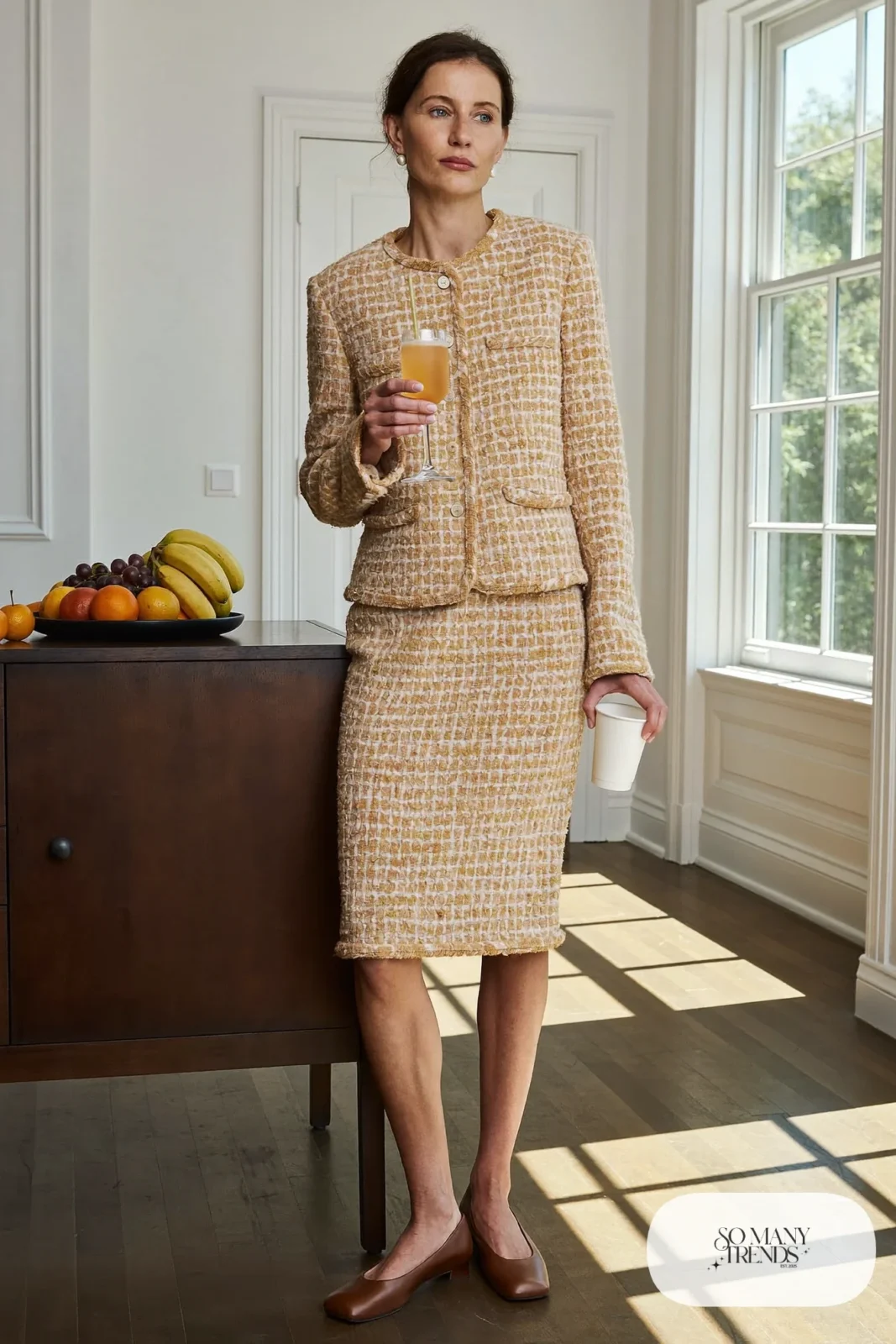 Woman in a sand and cream tweed skirt set with a white tee and low brown pumps at a brunch table, outfit 11