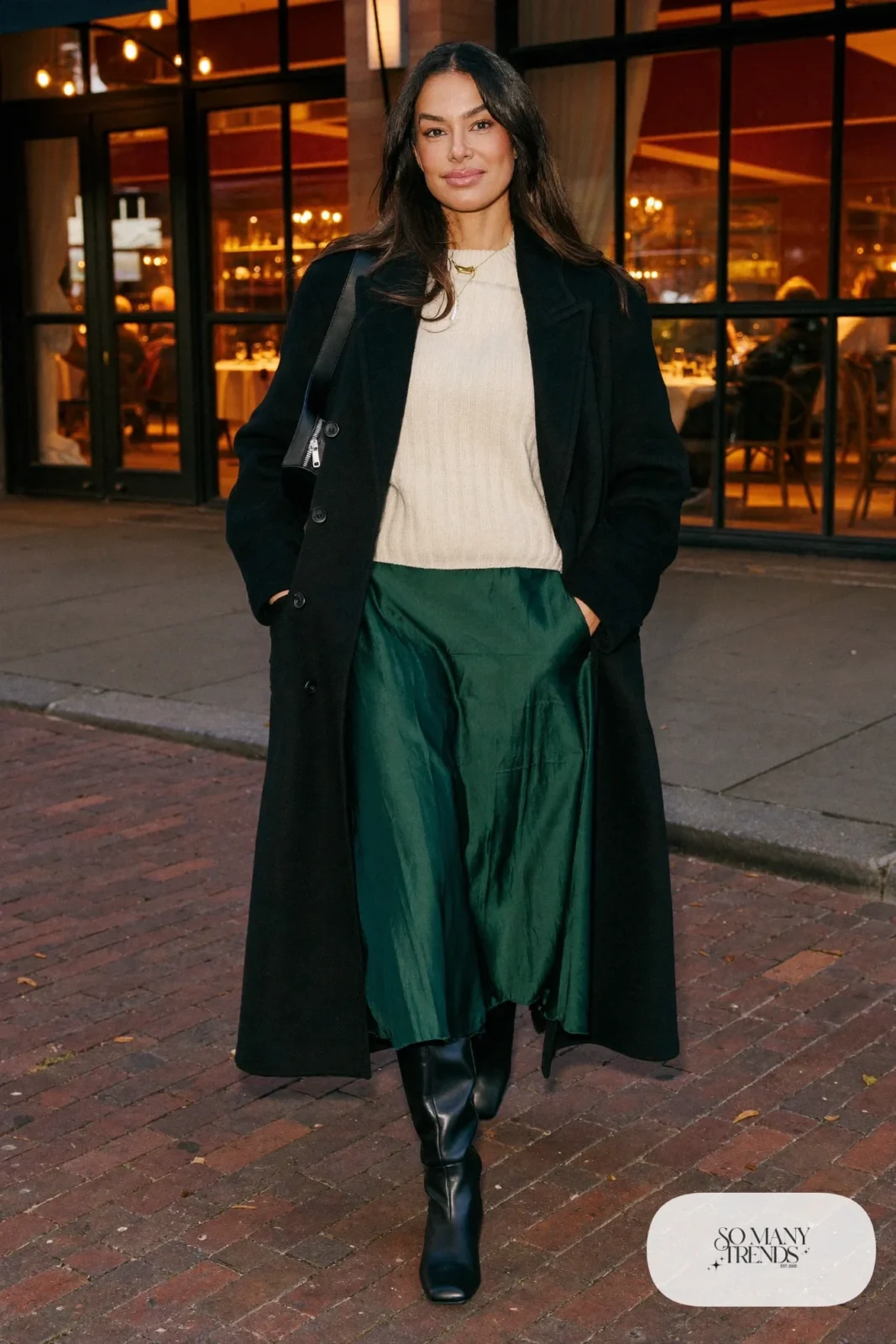 Woman in a forest green satin midi skirt, ivory sweater, tall black boots, tights and a black coat in Georgetown, outfit 21