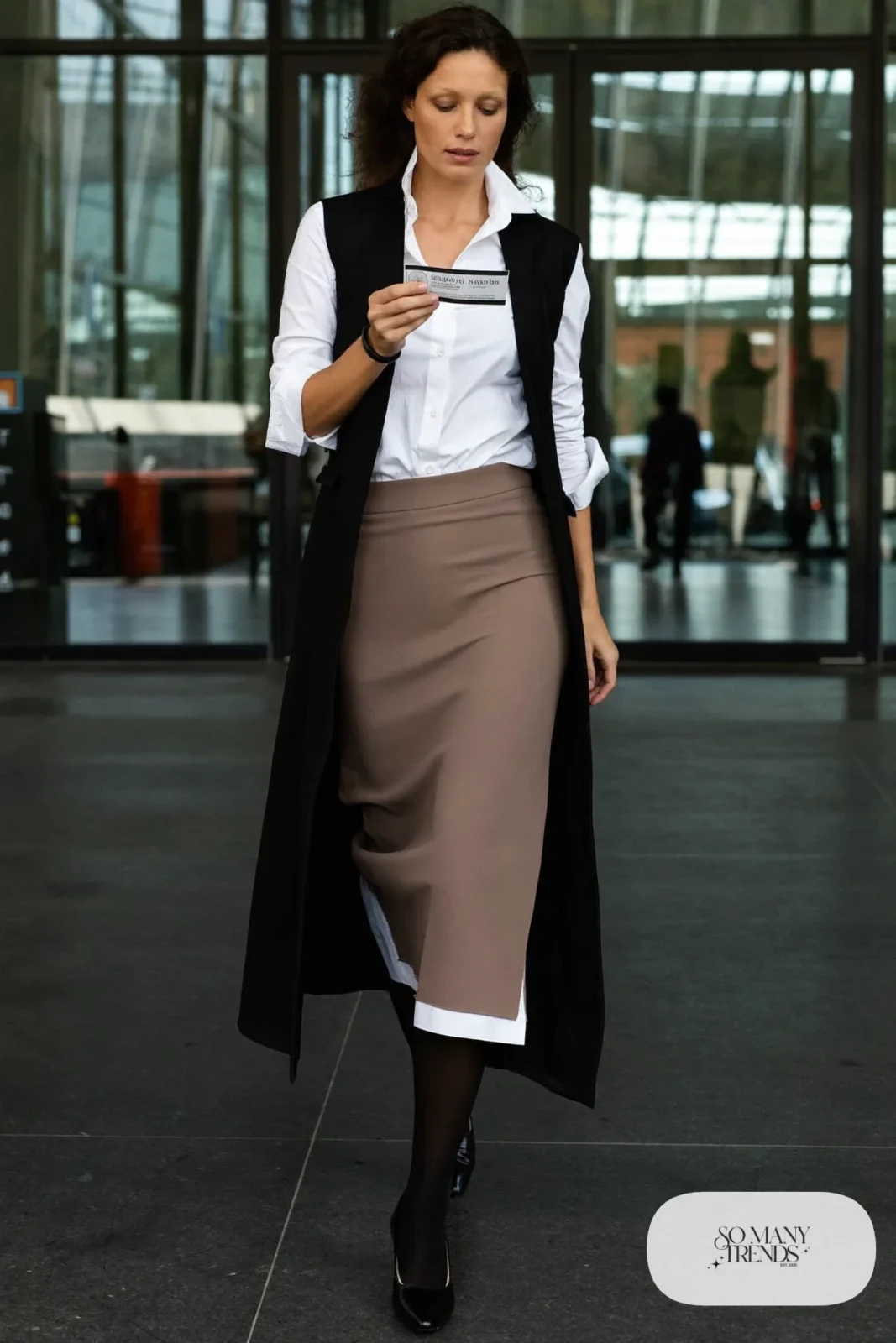 Black longline vest over white poplin shirt with taupe midi skirt and low-heel boots, outfit 18