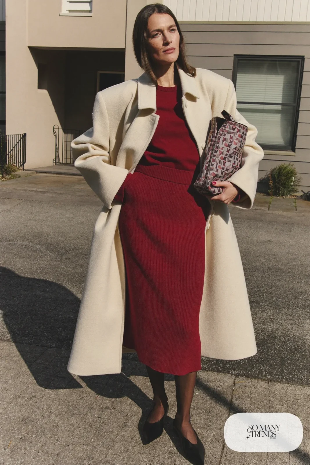 Woman in a burgundy ribbed knit midi dress, cream oversized coat, sheer black tights and black pointed flats, outfit 3