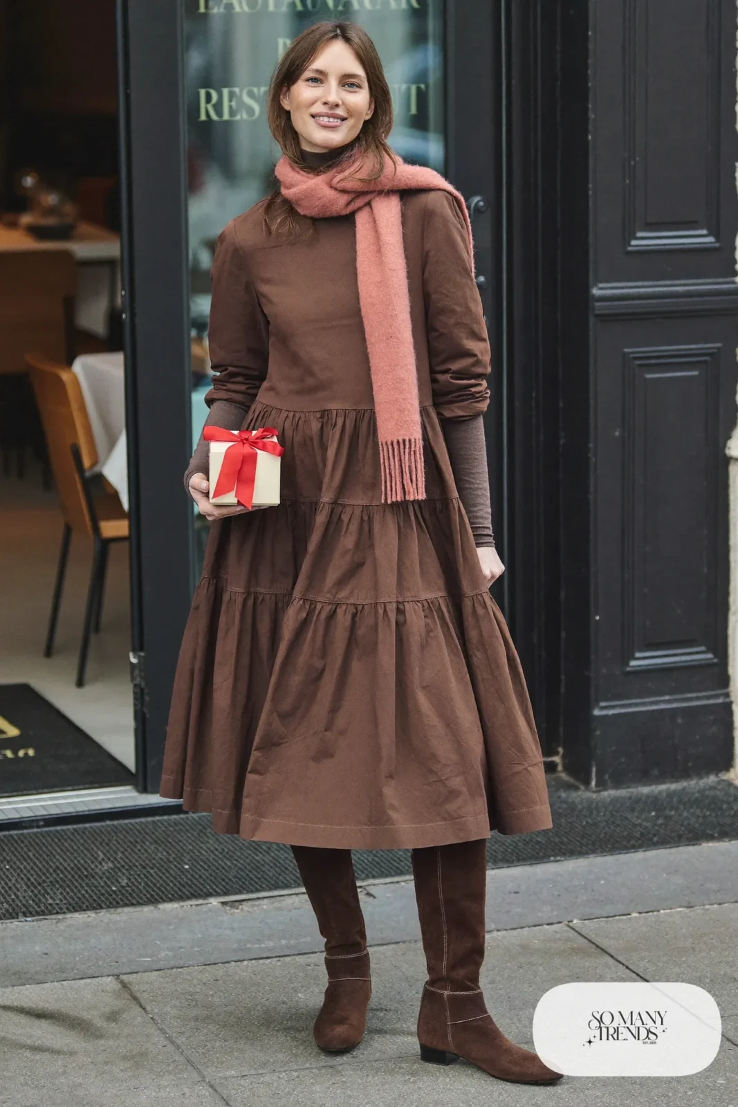 Woman in a chocolate brown tiered cotton midi dress, dusty pink scarf, brown tights and brown suede boots, outfit 6