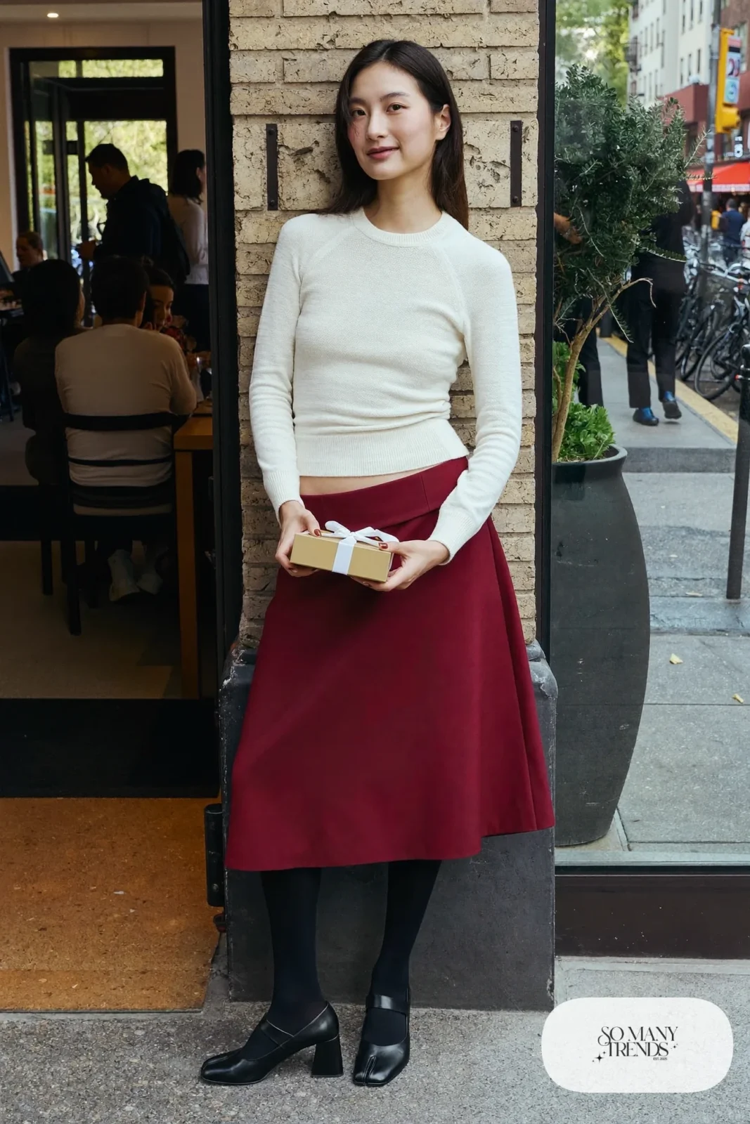 Woman in a cream fitted knit tucked into a burgundy A-line midi skirt, sheer black tights and black mary janes, outfit 14