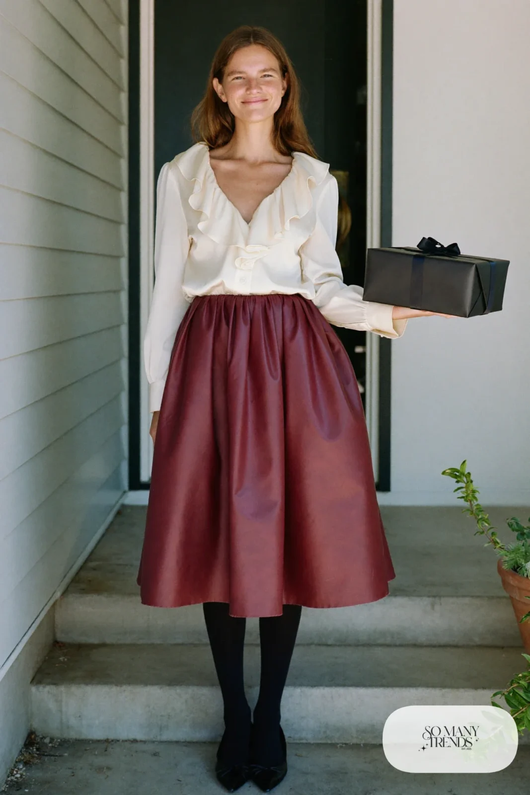 Woman in a cream ruffle-neck blouse, burgundy pleated midi skirt, black opaque tights and black pointed flats, outfit 16