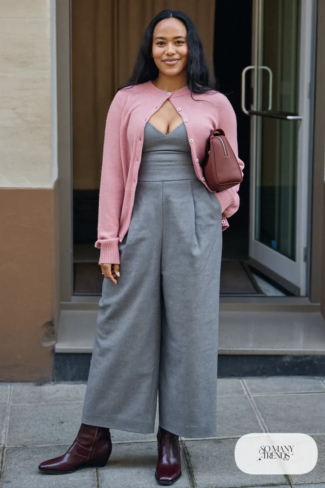 Woman in a gray wide-leg jumpsuit, dusty pink cardigan, burgundy ankle boots and brown bag, outfit 22