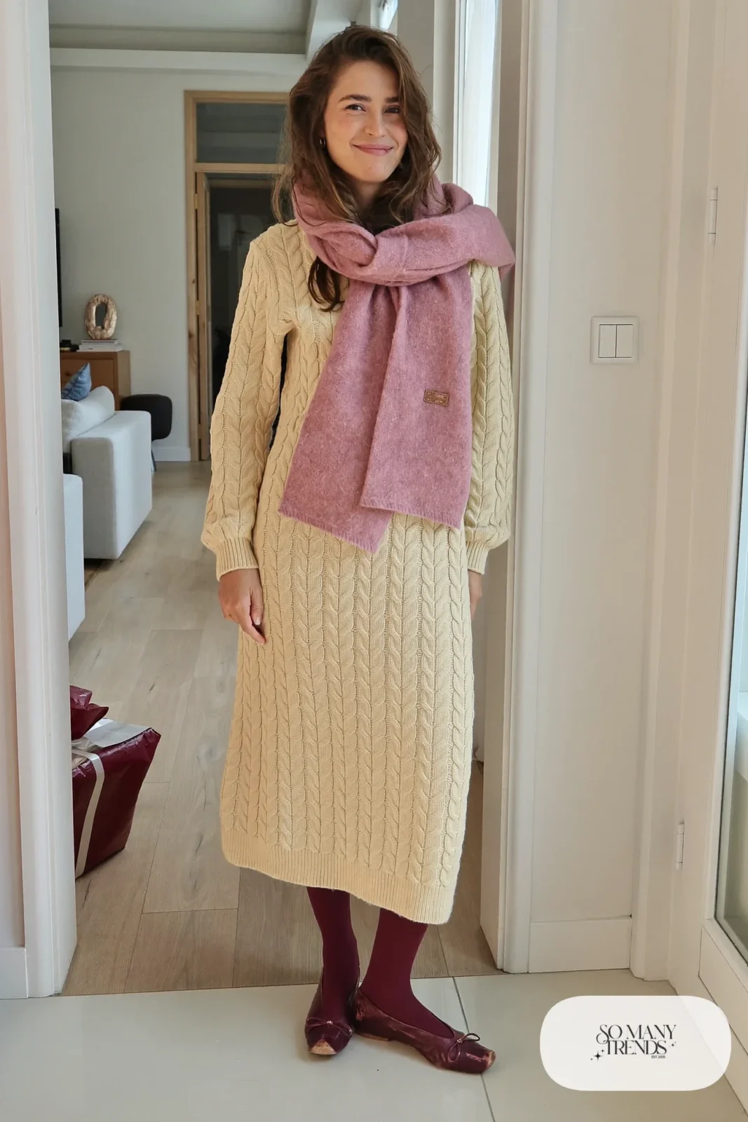 Woman in a cream cable-knit cardigan dress, dusty pink scarf, gray tights and burgundy flats, outfit 26