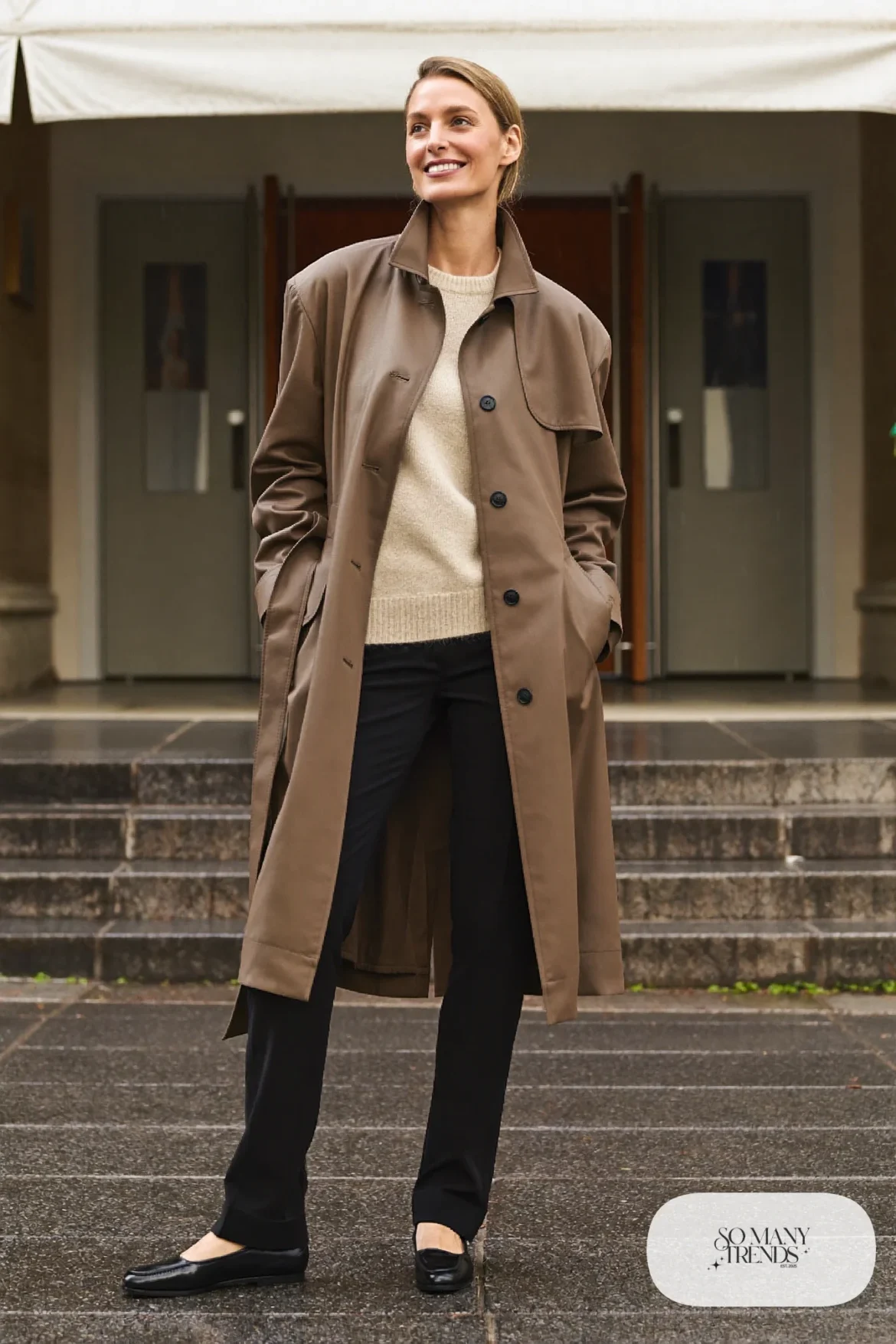 Taupe belted trench coat over champagne knit and straight black pants with loafers, outfit 13