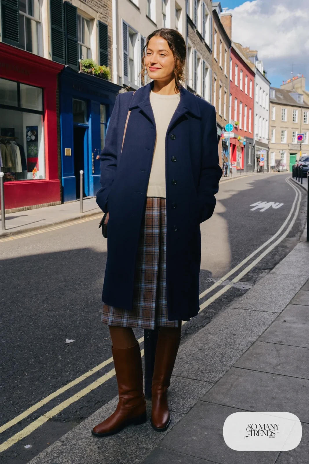 Woman in a navy wool pea coat, brown plaid wool midi skirt, cream knit sweater, brown opaque tights and tall brown boots in Edinburgh, outfit 2