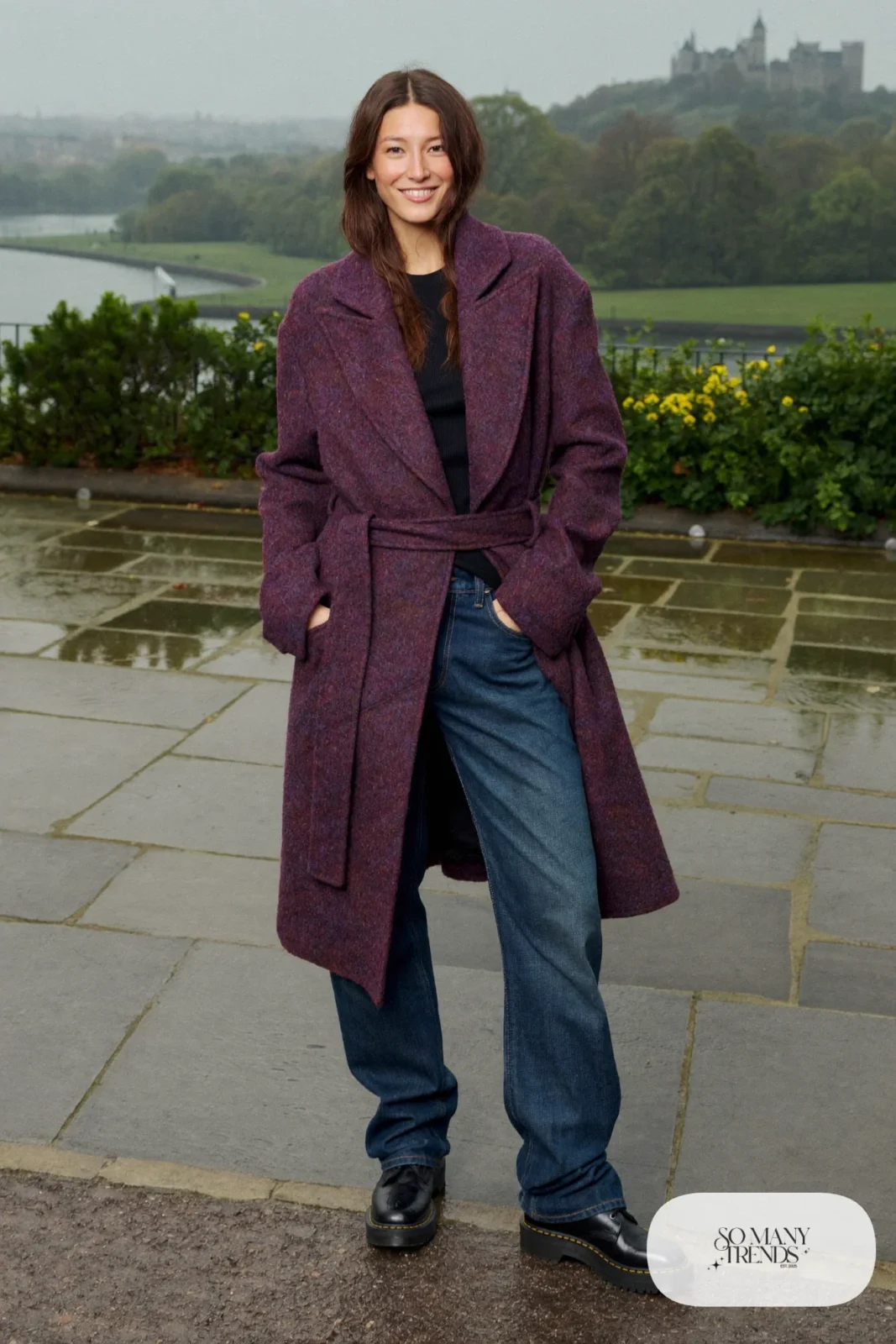 Woman in a heather plum belted wool wrap coat, black knit top, dark jeans and black leather boots on a rainy Edinburgh street, outfit 5