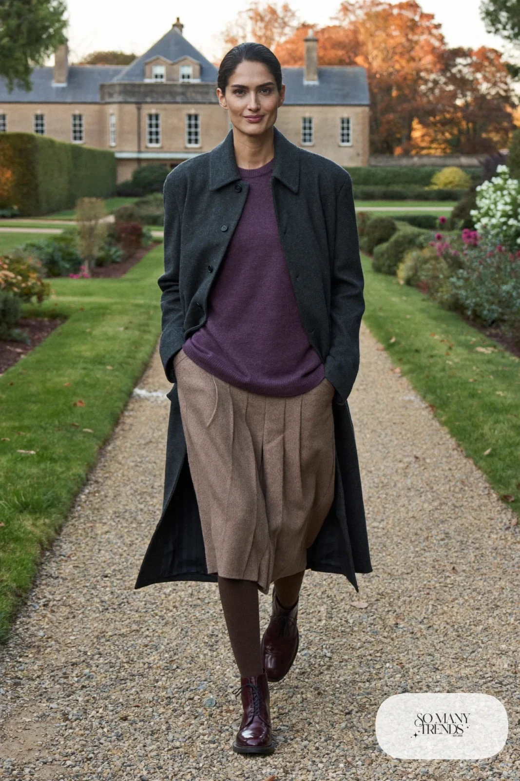 Woman in a heather plum knit sweater, sand pleated wool midi skirt, brown opaque tights and brown brogue boots in a heritage house garden, outfit 11